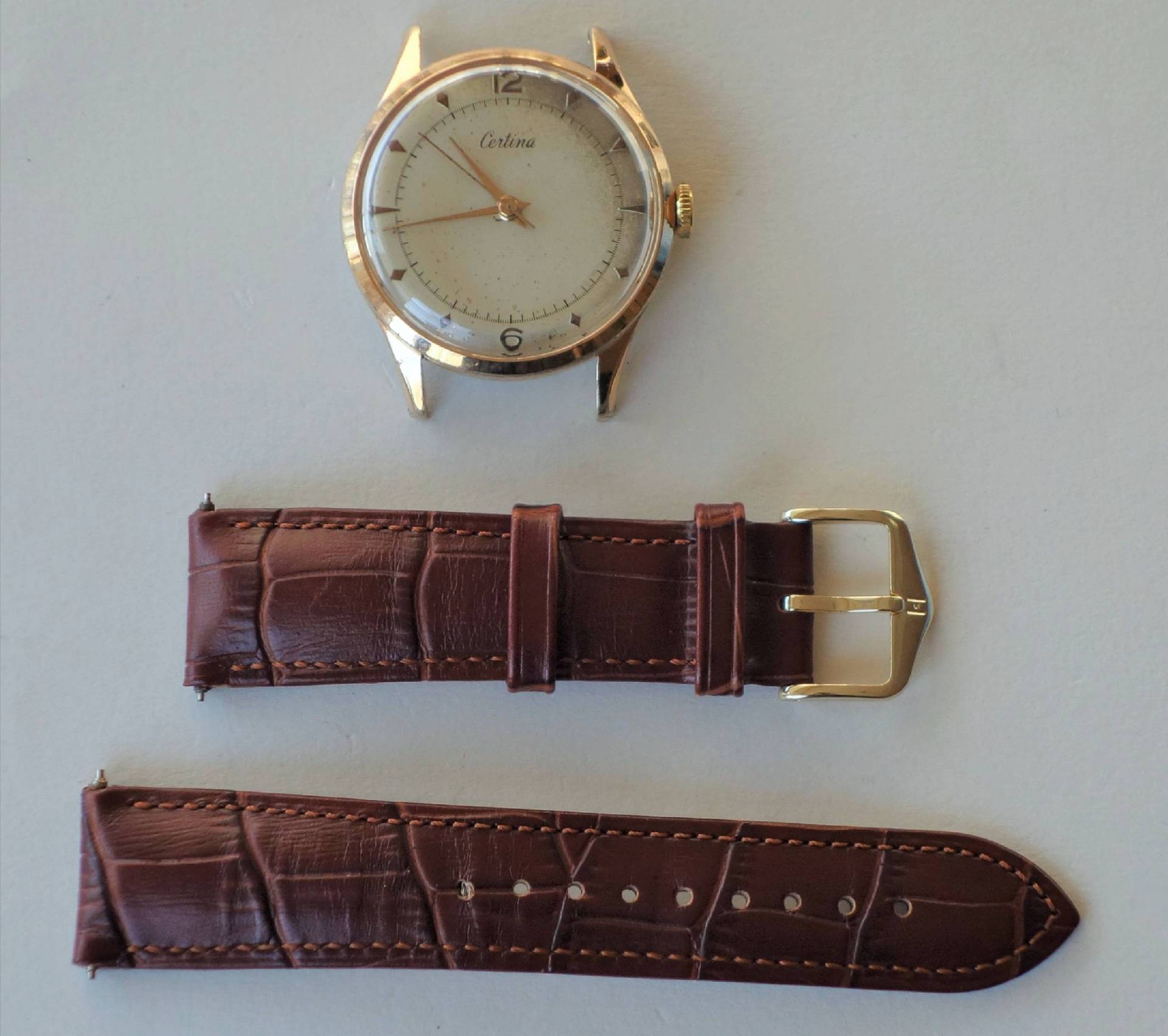 Zerlegte Armbanduhr mit goldfarbenem Gehäuse und braunem Armband in zwei Teilen.