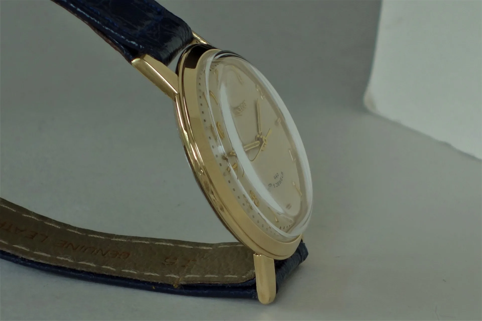 Goldfarbene Armbanduhr mit hellem Zifferblatt und dunkelblauem Lederarmband.