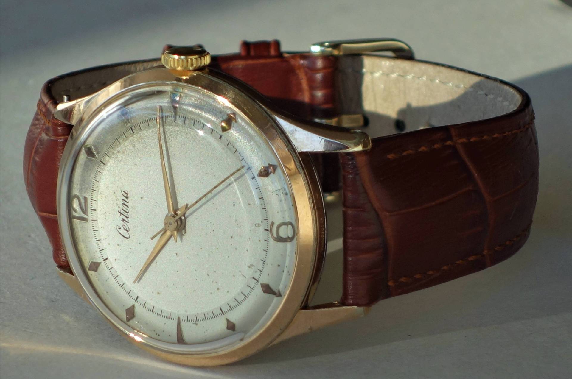 Analoge Armbanduhr mit braunem Armband und goldfarbenem Gehäuse.