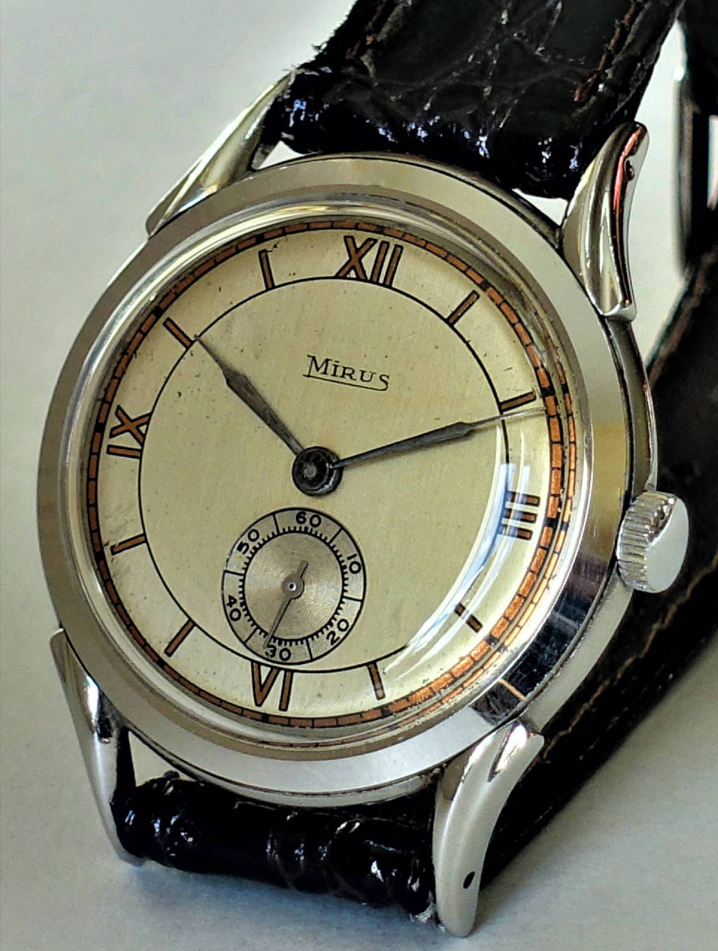 Analoge Armbanduhr mit beigem Zifferblatt, römischen Ziffern und schwarzem Armband.