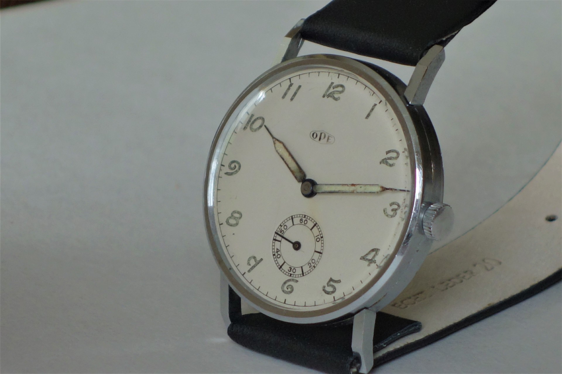 Analoge Armbanduhr mit weißem Zifferblatt, schwarzen Zahlen und schwarzem Armband.