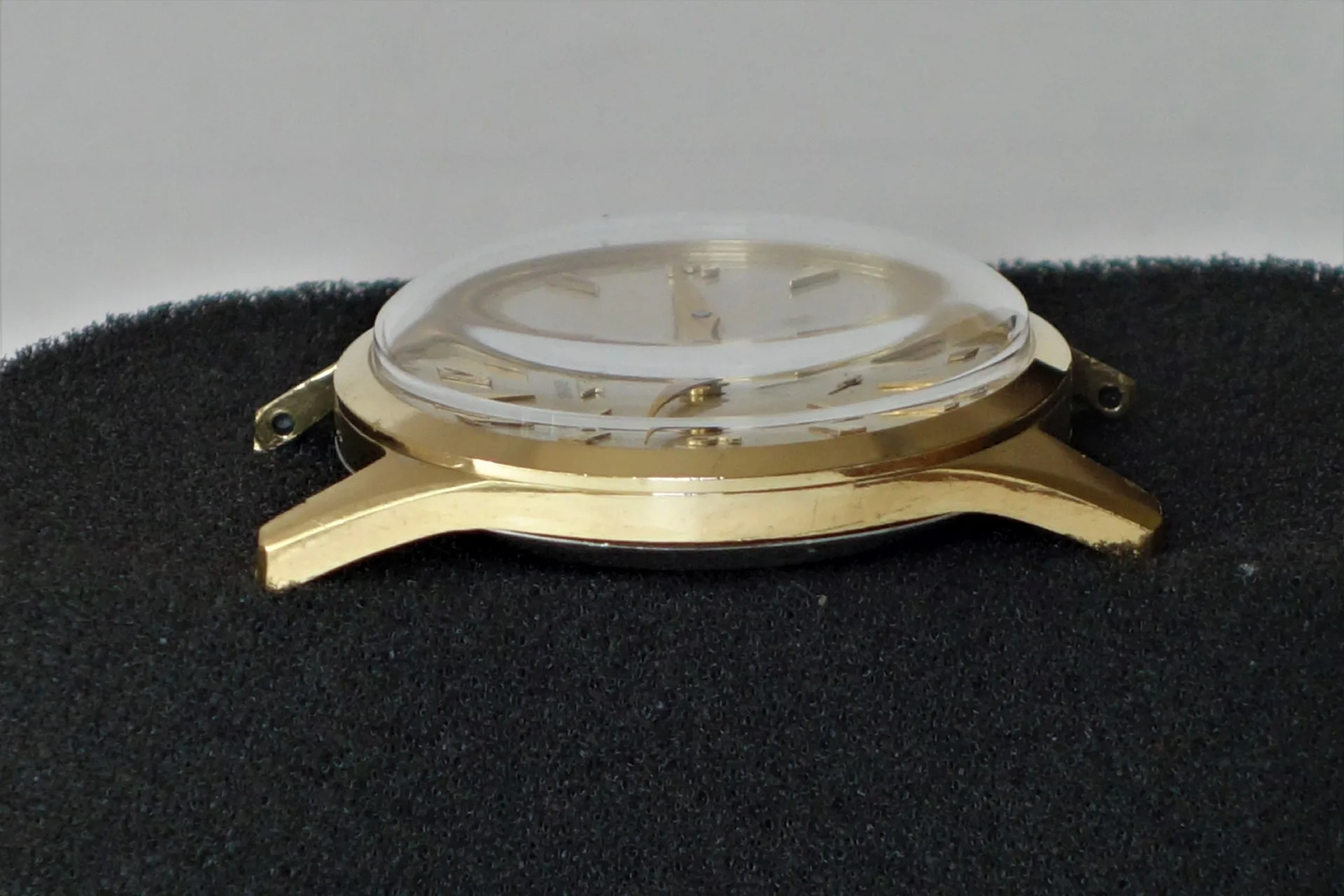 Goldfarbenes Uhrgehäuse mit montiertem Glas und Zifferblatt ohne Armband.