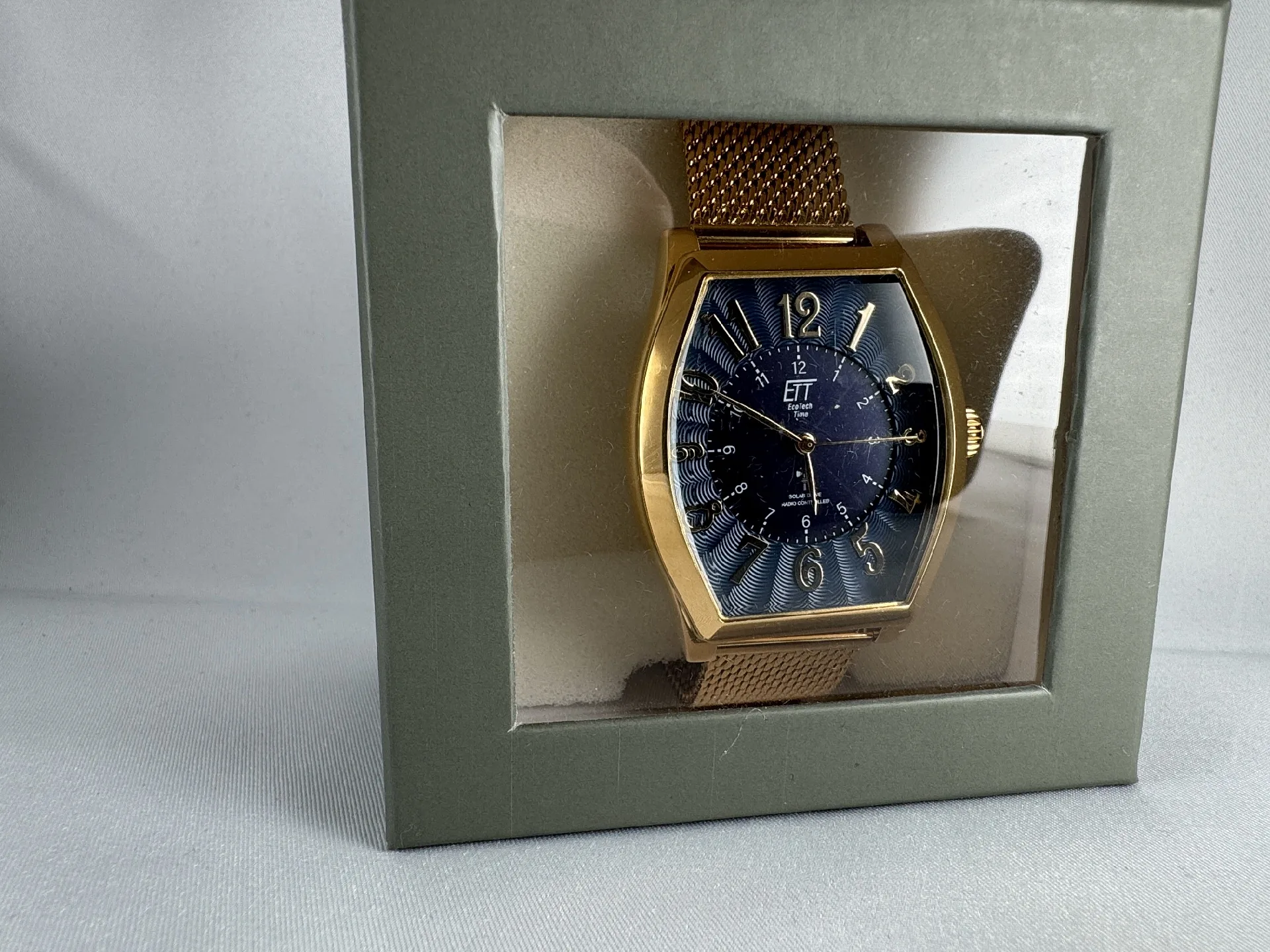 Goldene Armbanduhr mit Meshband Goldfarbene Armbanduhr mit blauem Zifferblatt und Metall-Mesharmband in Geschenkbox.
