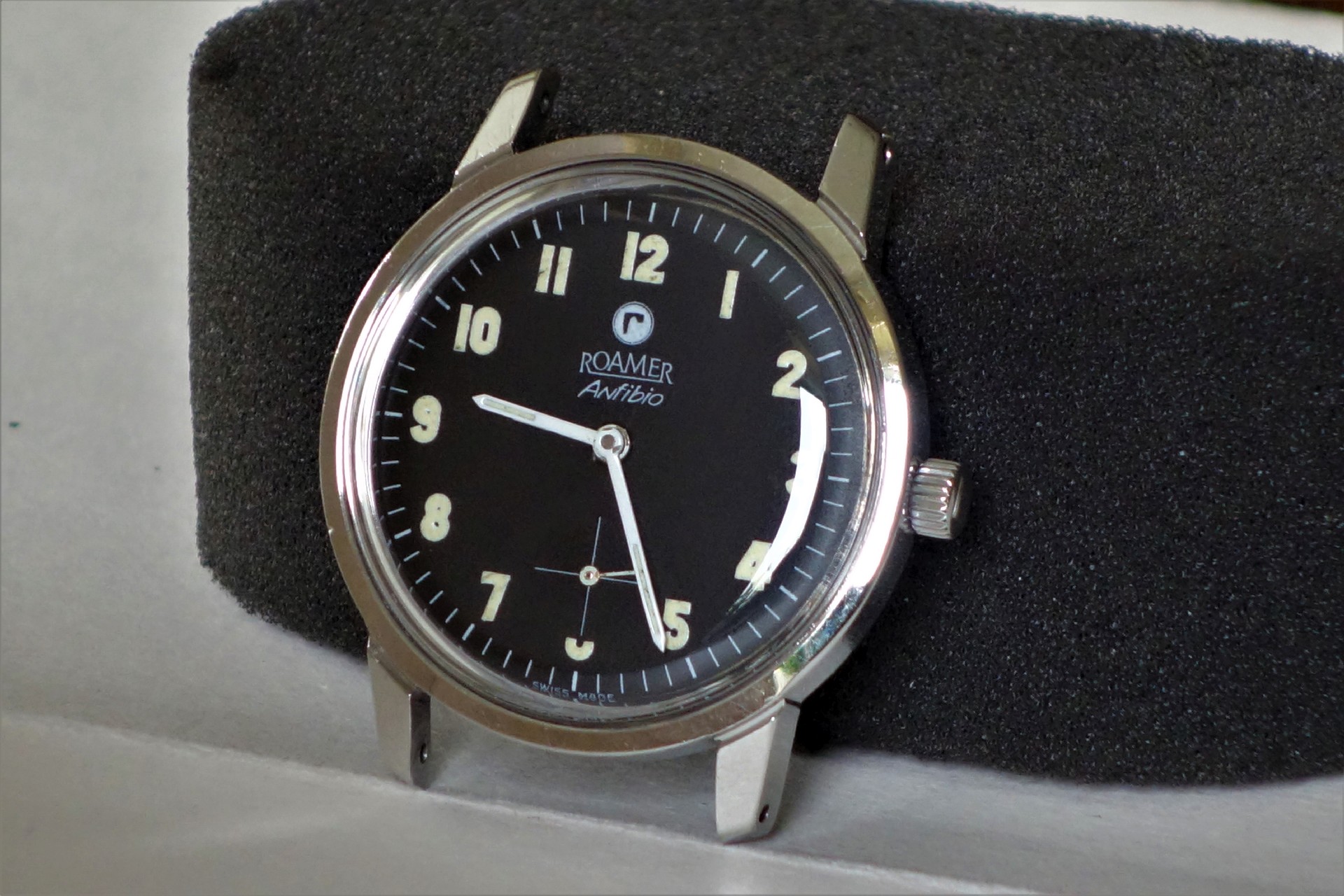 Schwarze analoge Armbanduhr mit silberfarbenem Gehäuse und Leuchtziffern.