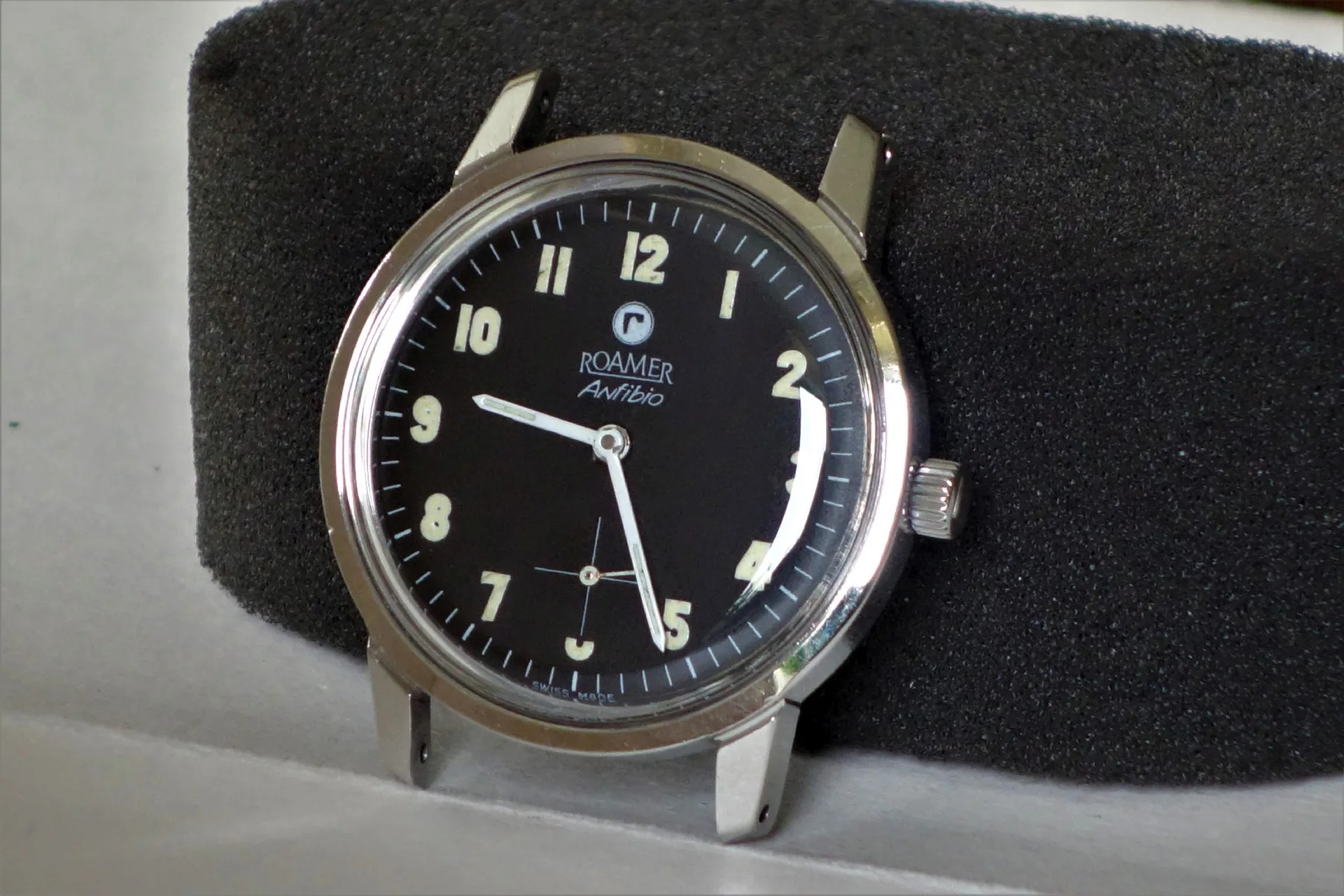 Schwarze analoge Armbanduhr mit silberfarbenem Gehäuse und Leuchtziffern.