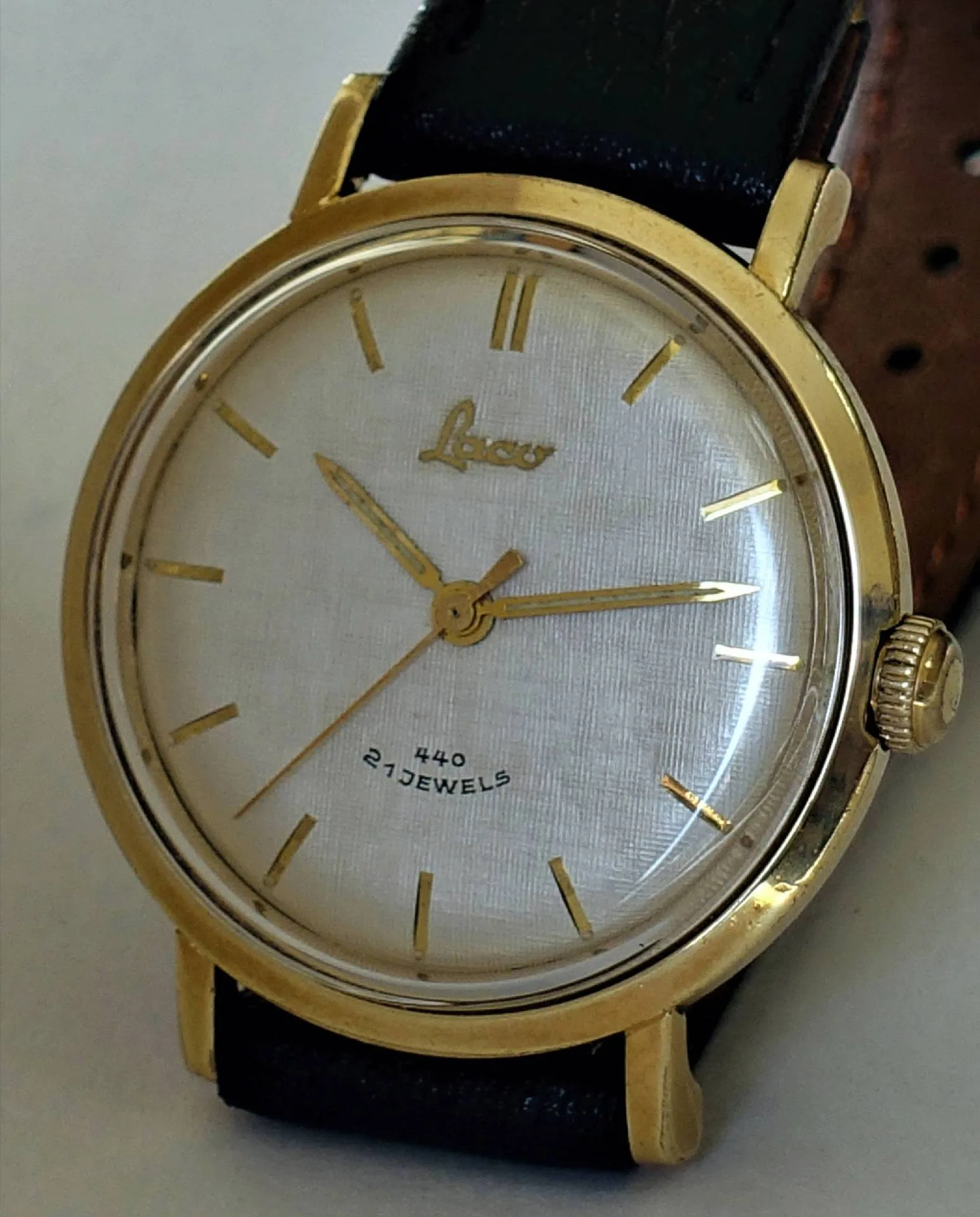 Goldfarbene Armbanduhr mit weißem Zifferblatt, goldenen Zeigern und schwarzem Armband.
