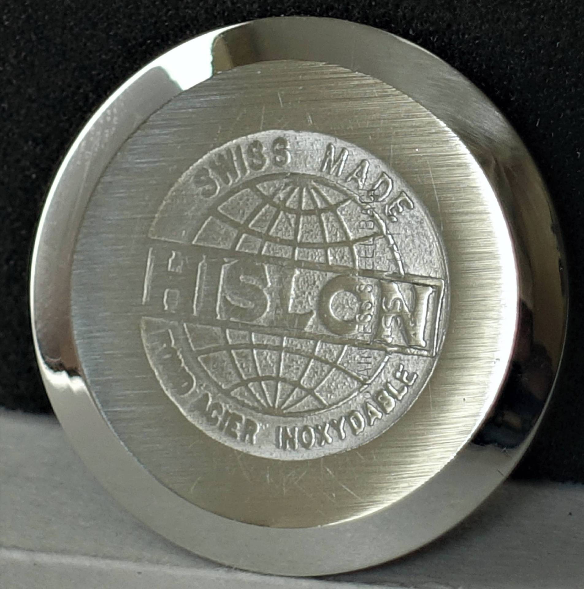 Runder, silberfarbener Uhrenboden mit HISLON-Logo und Gravur "Swiss Made" sowie einer stilisierten Weltkugel.
