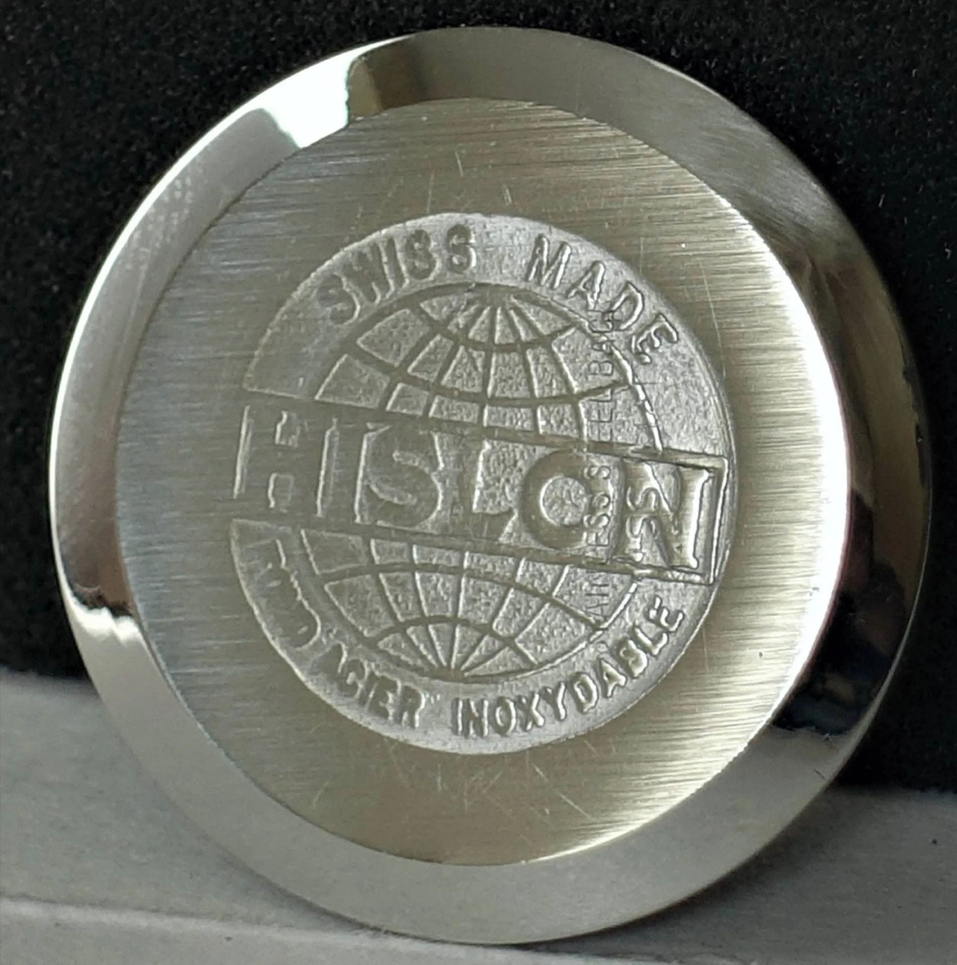 Silberfarbener HISLON Uhrenboden rund Runder, silberfarbener Uhrenboden mit HISLON-Logo und Gravur "Swiss Made" sowie einer stilisierten Weltkugel.