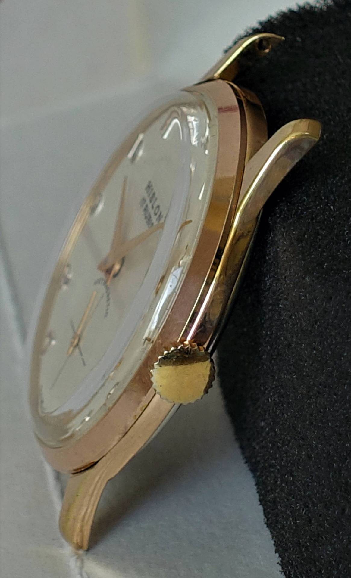 Eine Armbanduhr mit rosé-goldenem Gehäuse, cremefarbenem Zifferblatt und goldfarbenen Zeigern liegt seitlich auf einem schwarzen Kissen.