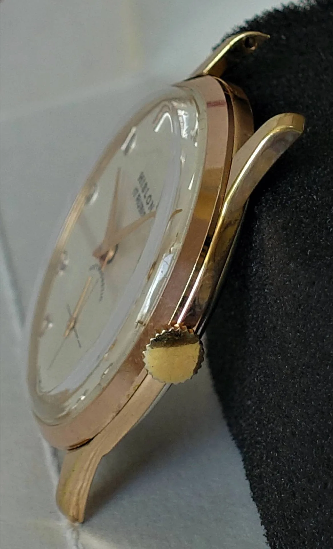 Rosé-goldene Uhr mit cremefarbenem Zifferblatt Eine Armbanduhr mit rosé-goldenem Gehäuse, cremefarbenem Zifferblatt und goldfarbenen Zeigern liegt seitlich auf einem schwarzen Kissen.