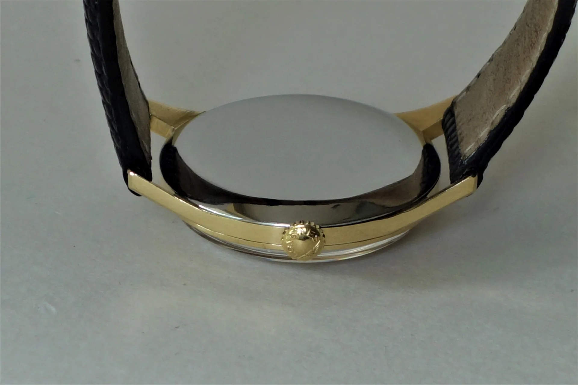 Rundes Uhrengehäuse mit silberfarbener Rückseite und goldfarbener Krone, an schwarzem Armband.
