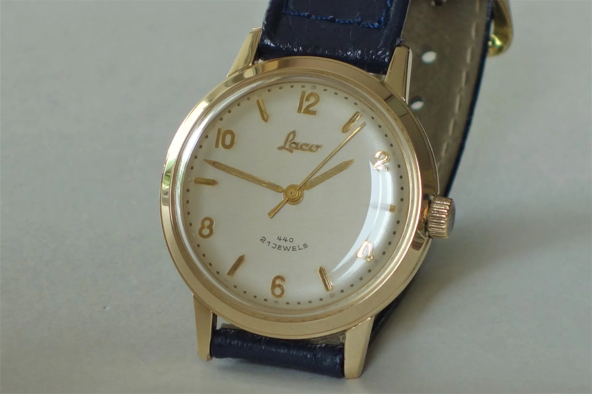 Analoge Armbanduhr mit goldfarbenem Gehäuse, hellem Zifferblatt und dunklem Armband.