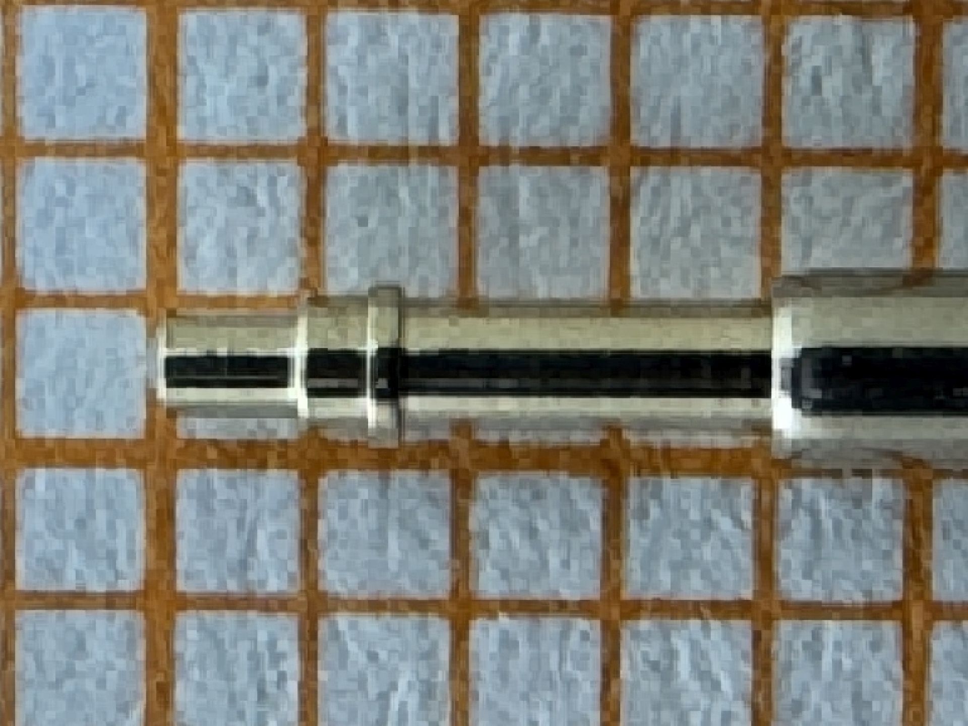 Metallische Wellenachse eines Uhrwerks auf kariertem Untergrund.