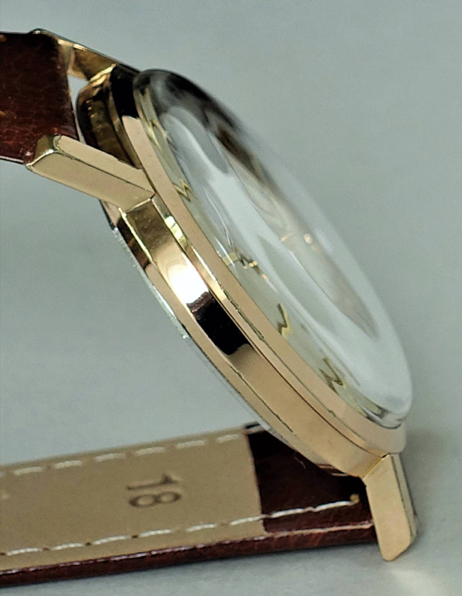 Flache Armbanduhr mit goldfarbenem Gehäuse und braunem Lederarmband.