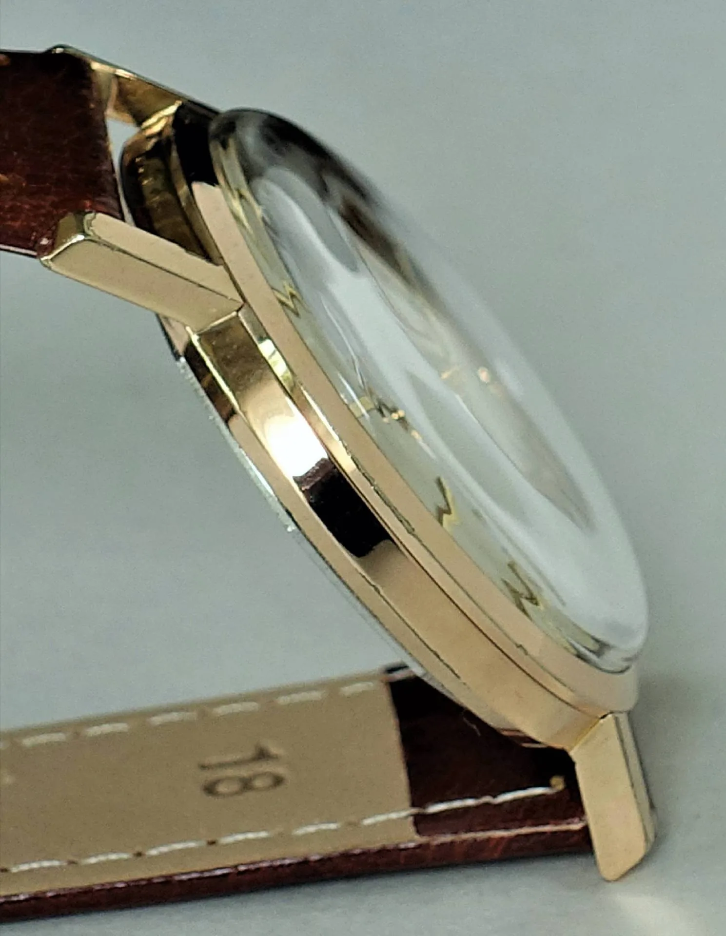 Flache Armbanduhr mit goldfarbenem Gehäuse und braunem Lederarmband.