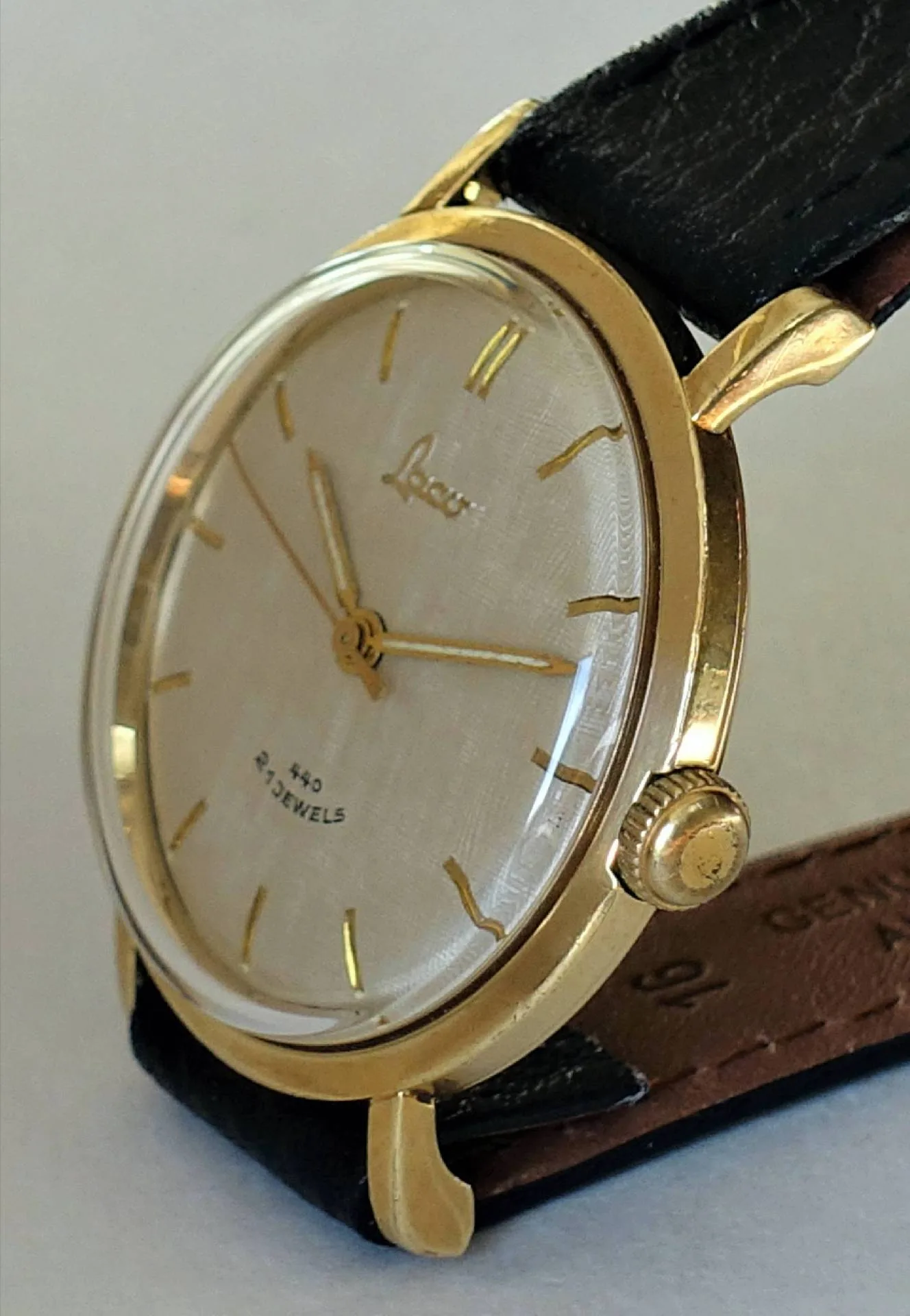 Analoge Armbanduhr mit goldfarbenem Gehäuse, hellem Zifferblatt und schwarzem Armband.