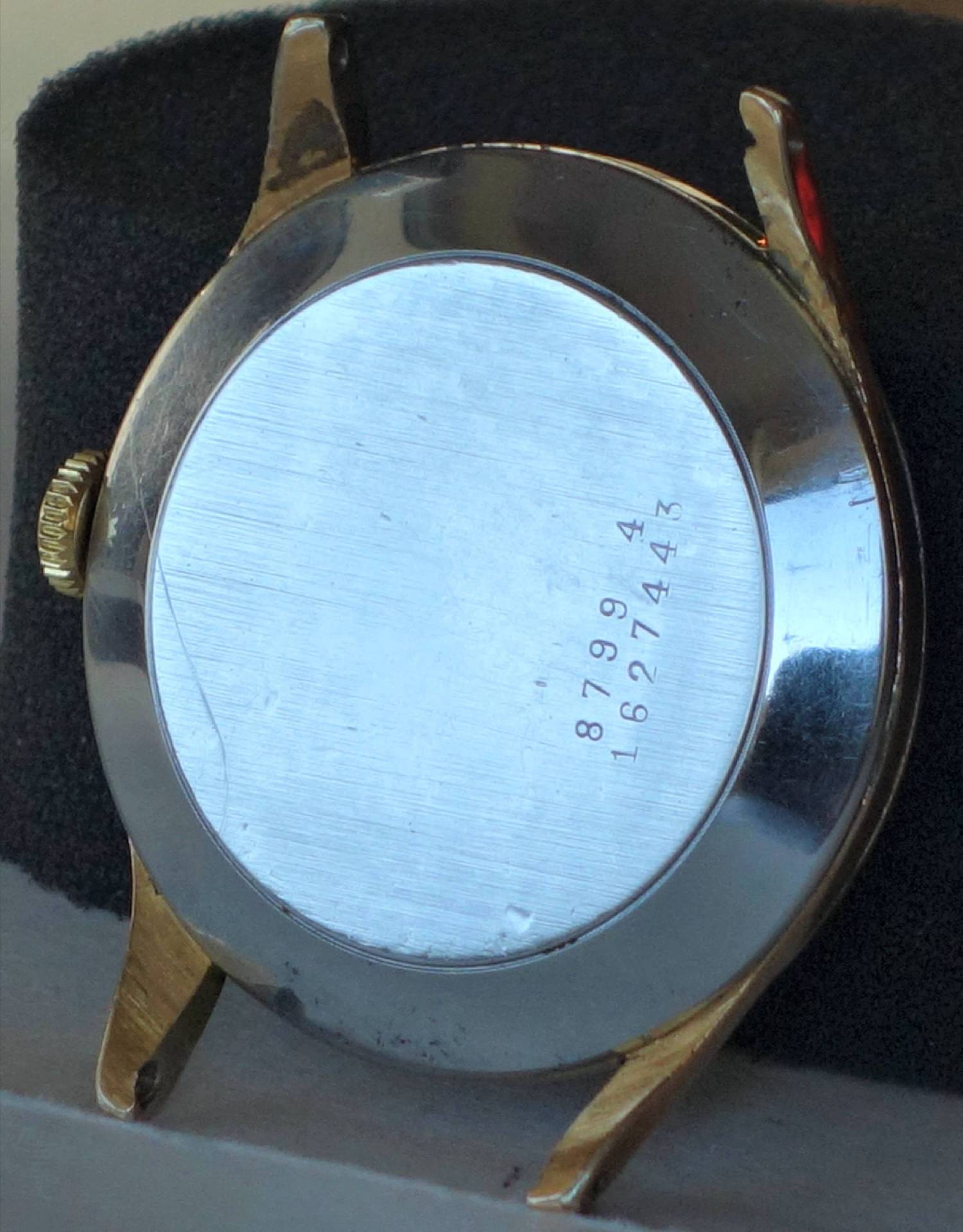 Rundes Uhrengehäuse in silberner und goldfarbener Optik mit glattem Metallboden und seitlicher Krone.