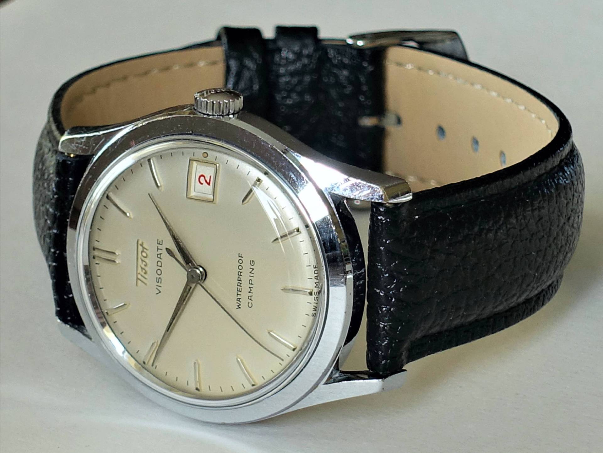 Silberfarbene Armbanduhr mit hellem Zifferblatt und schwarzem Lederarmband.