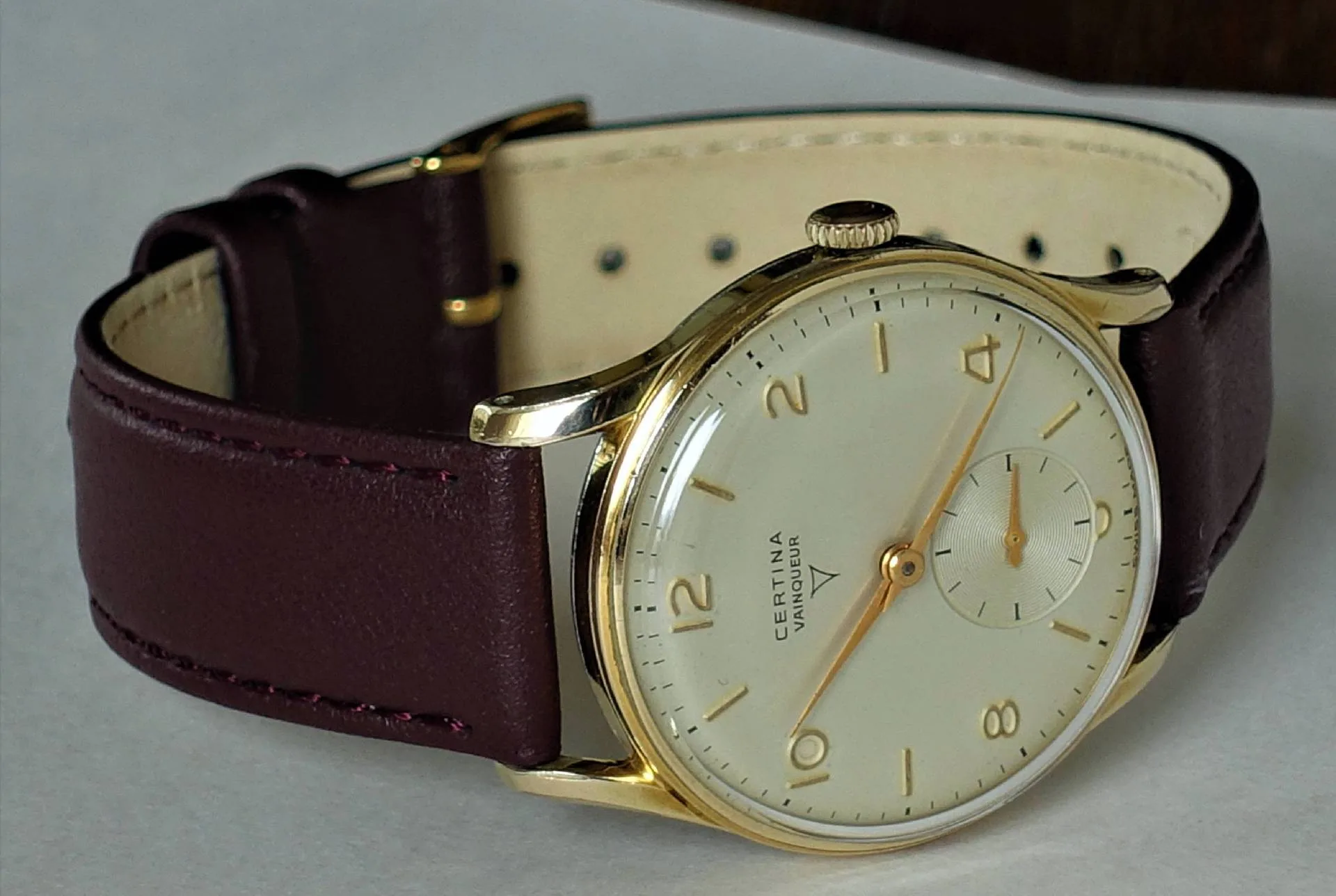 Analoge Armbanduhr mit goldfarbenem Gehäuse, hellem Zifferblatt und dunkelbraunem Lederarmband.