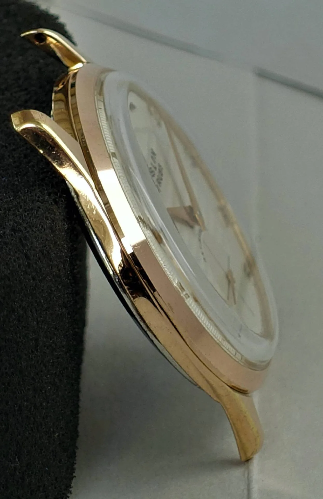 Das Bild zeigt ein seitlich aufgenommenes, poliert roségoldfarbenes Uhrengehäuse mit weißem Zifferblatt und goldfarbenen Zeigern.