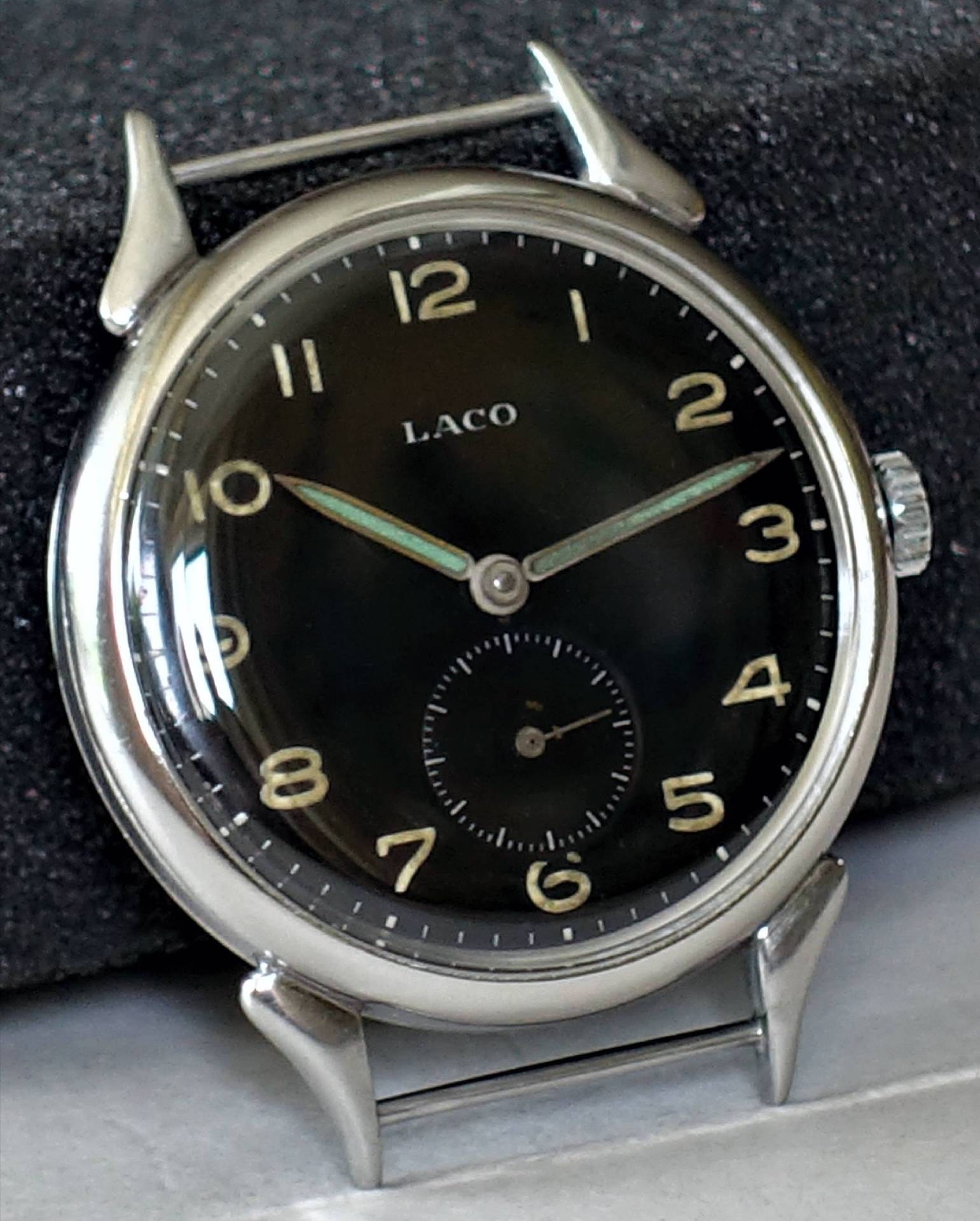 Schwarze Armbanduhr mit silberfarbenem Gehäuse und Leuchtzeigern, Zifferblatt mit arabischen Zahlen und kleiner Sekunde.