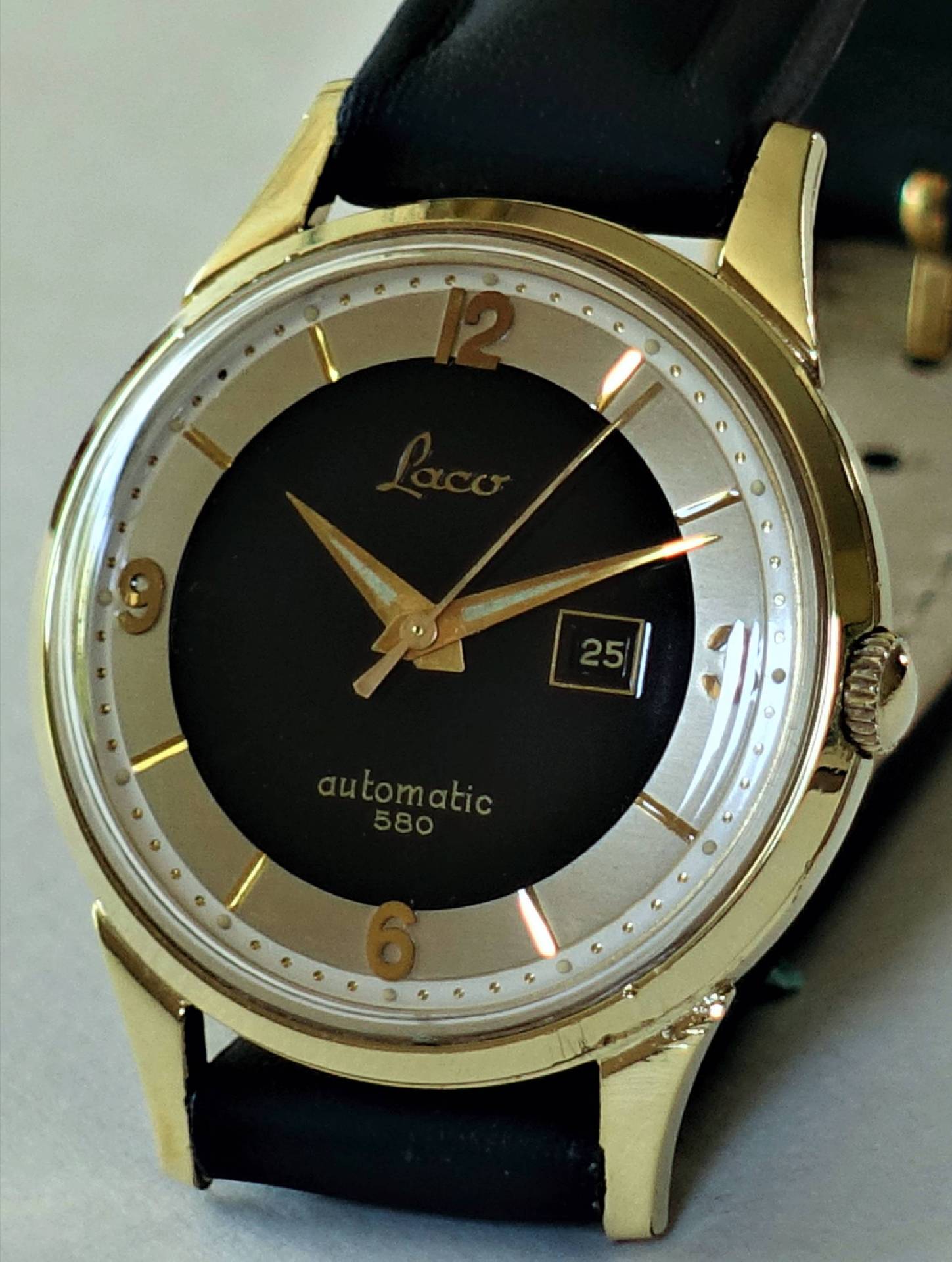 Goldfarbene Armbanduhr mit schwarzem Zifferblatt, Datumsanzeige und schwarzem Armband.