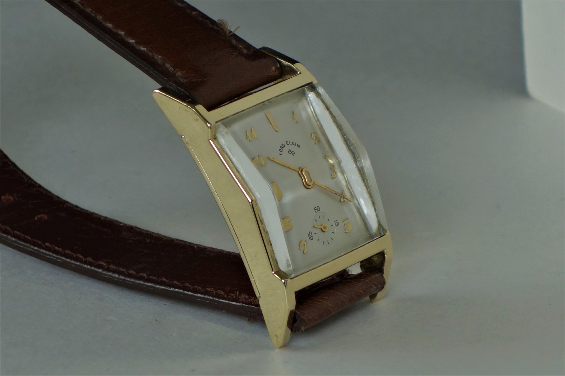 Rechteckige Armbanduhr mit goldfarbenem Gehäuse und braunem Armband.