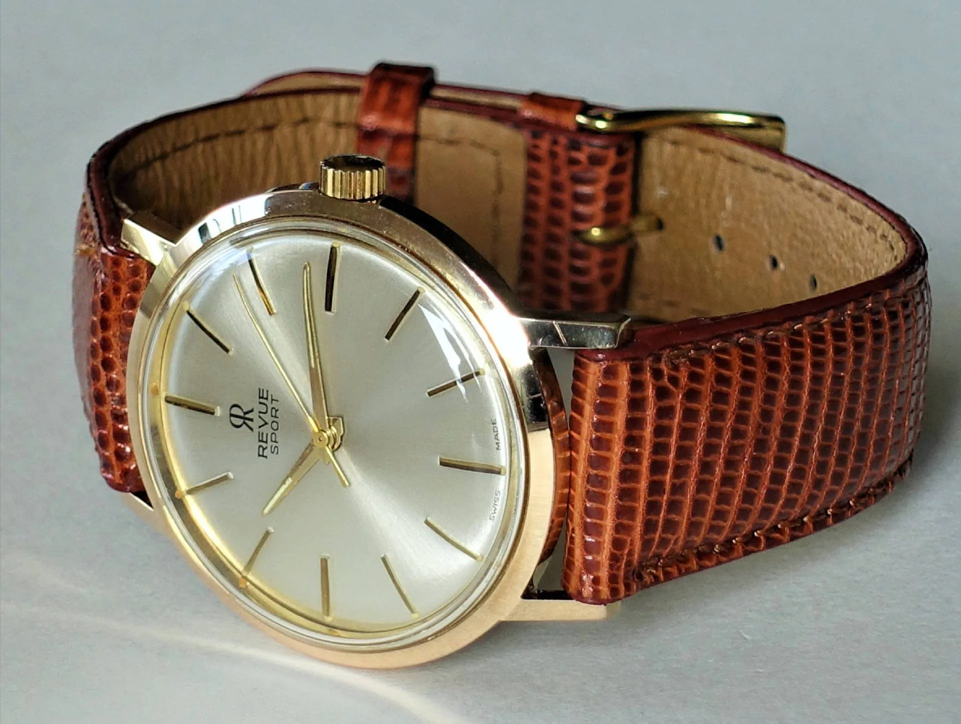 Revue Sport Armbanduhr Klassische Armbanduhr mit hellem Zifferblatt, goldfarbenem Gehäuse und braunem Lederarmband.