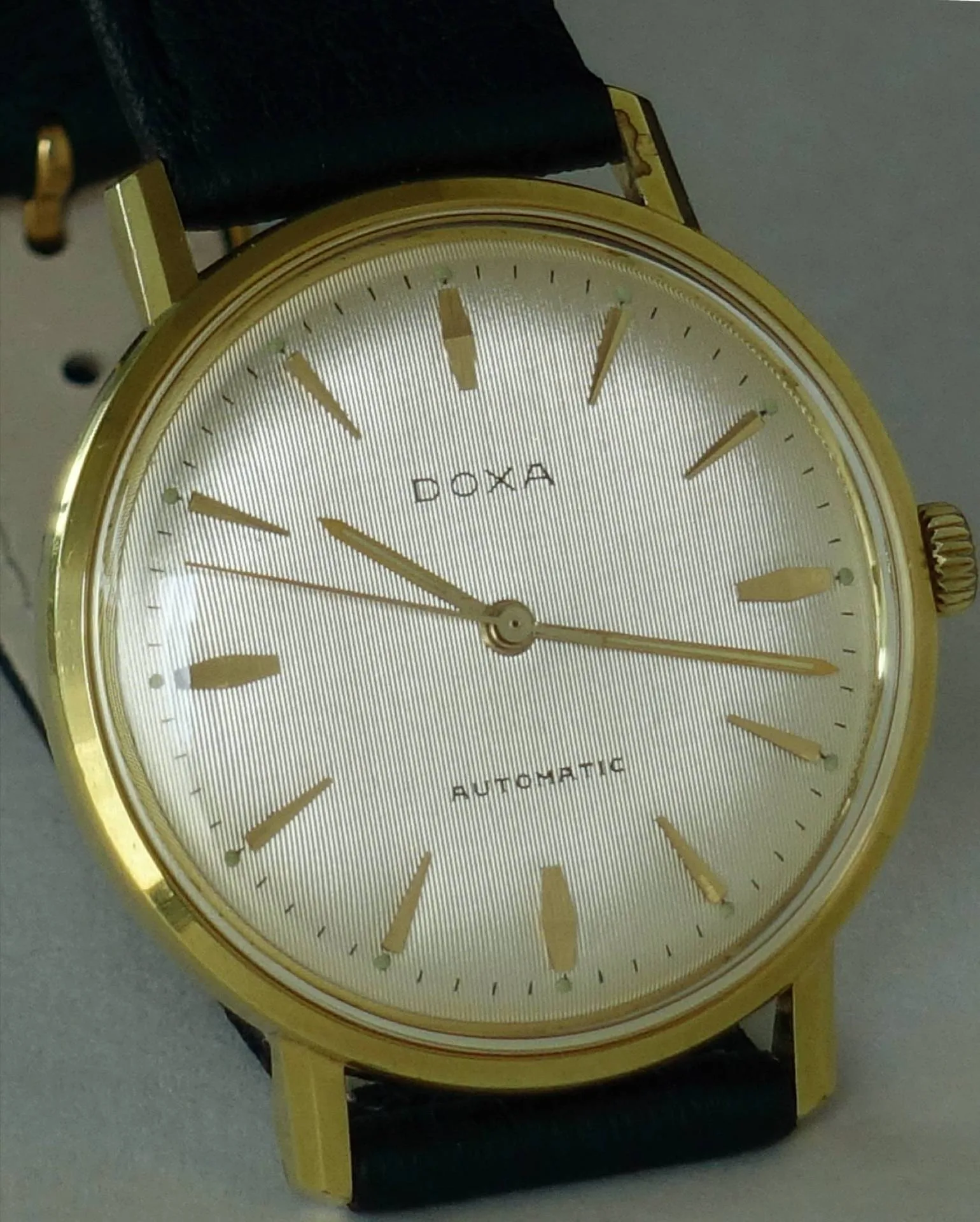 Doxa Armbanduhr goldfarben Goldfarbene Doxa Armbanduhr mit hellem Zifferblatt und schwarzem Armband.