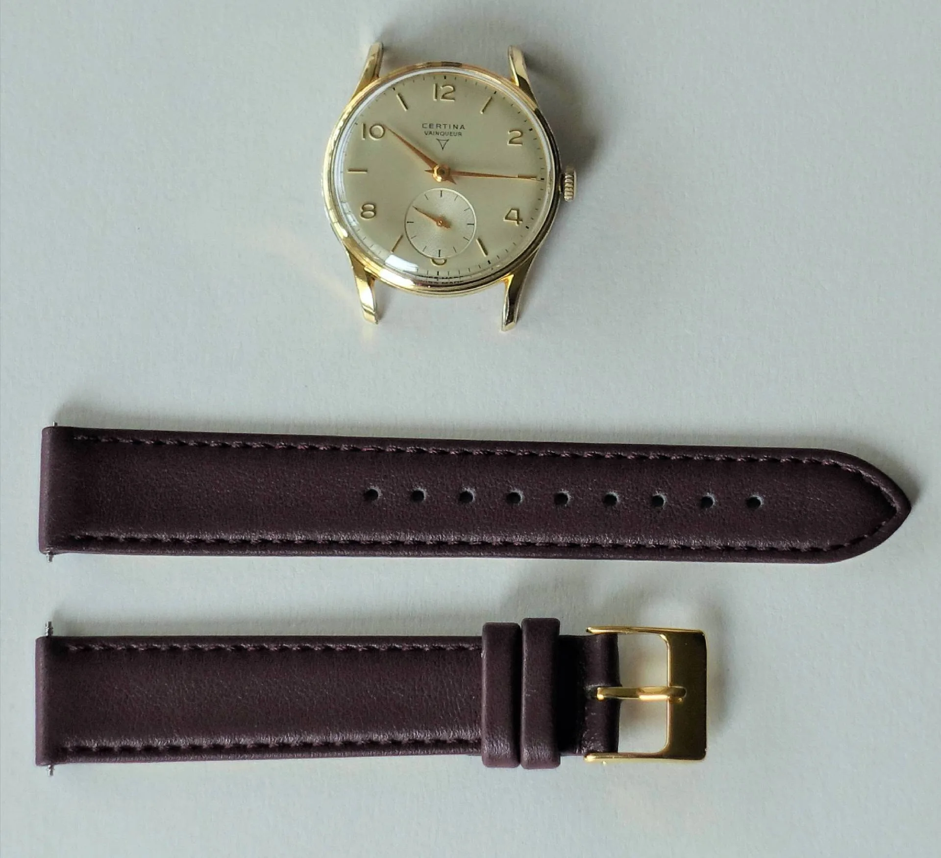 Runde Armbanduhr mit hellem Zifferblatt und braunem Lederarmband mit goldfarbener Schließe.
