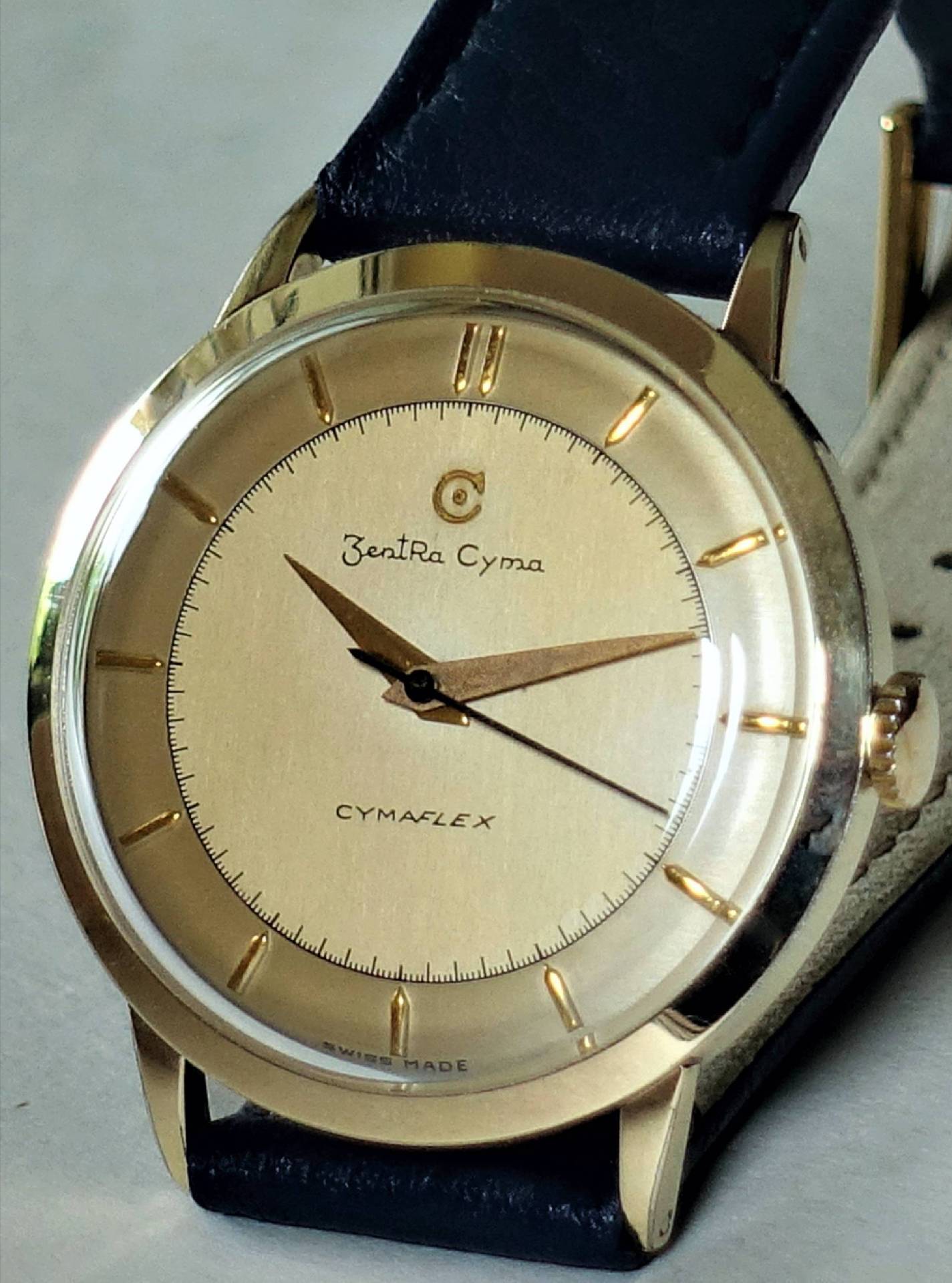 Goldfarbene Armbanduhr mit hellem Zifferblatt und schwarzem Armband.