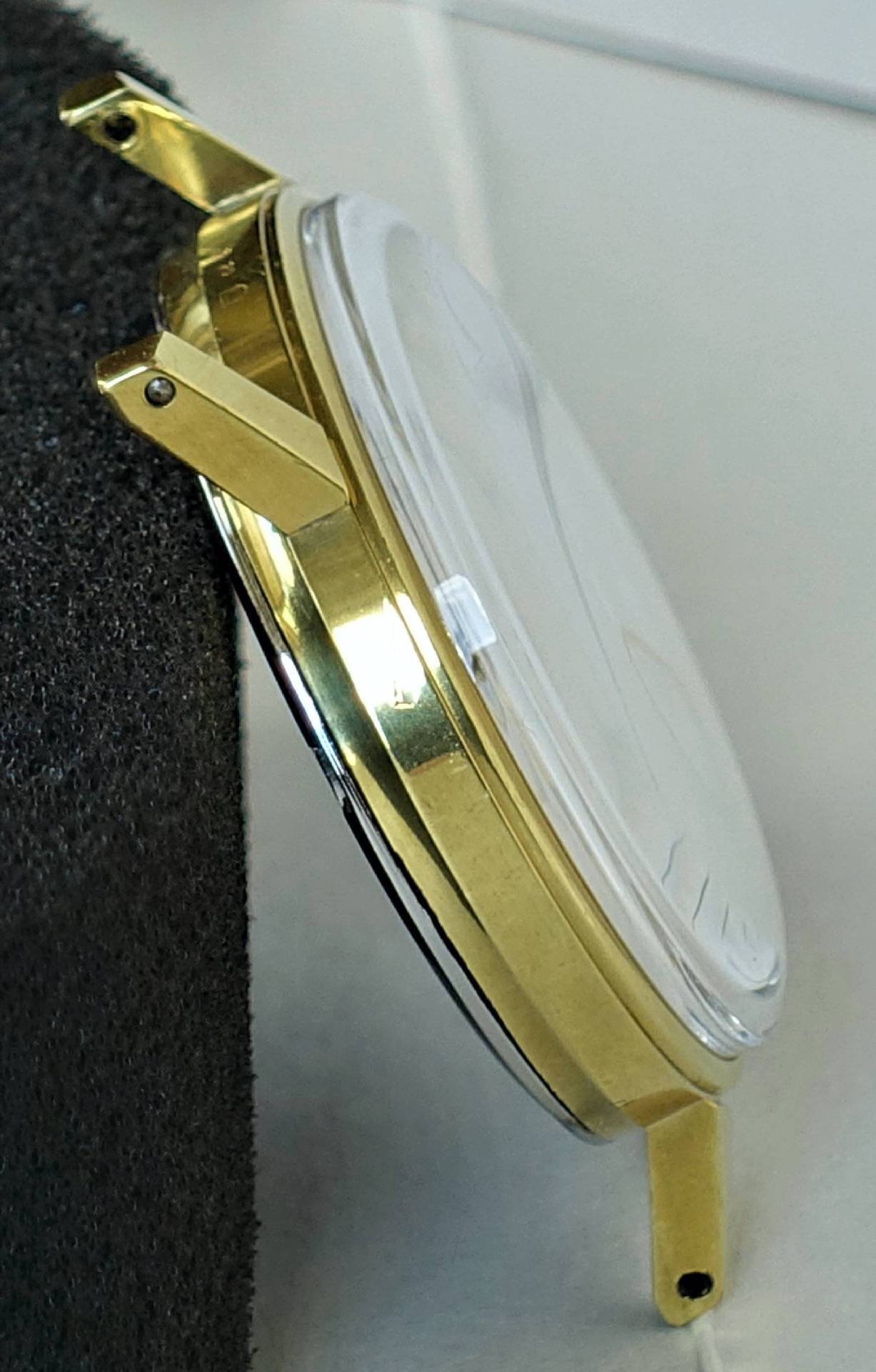 Rundes Uhrgehäuse in goldfarbener Optik mit angesetzten Bandanstößen und transparentem Uhrglas.