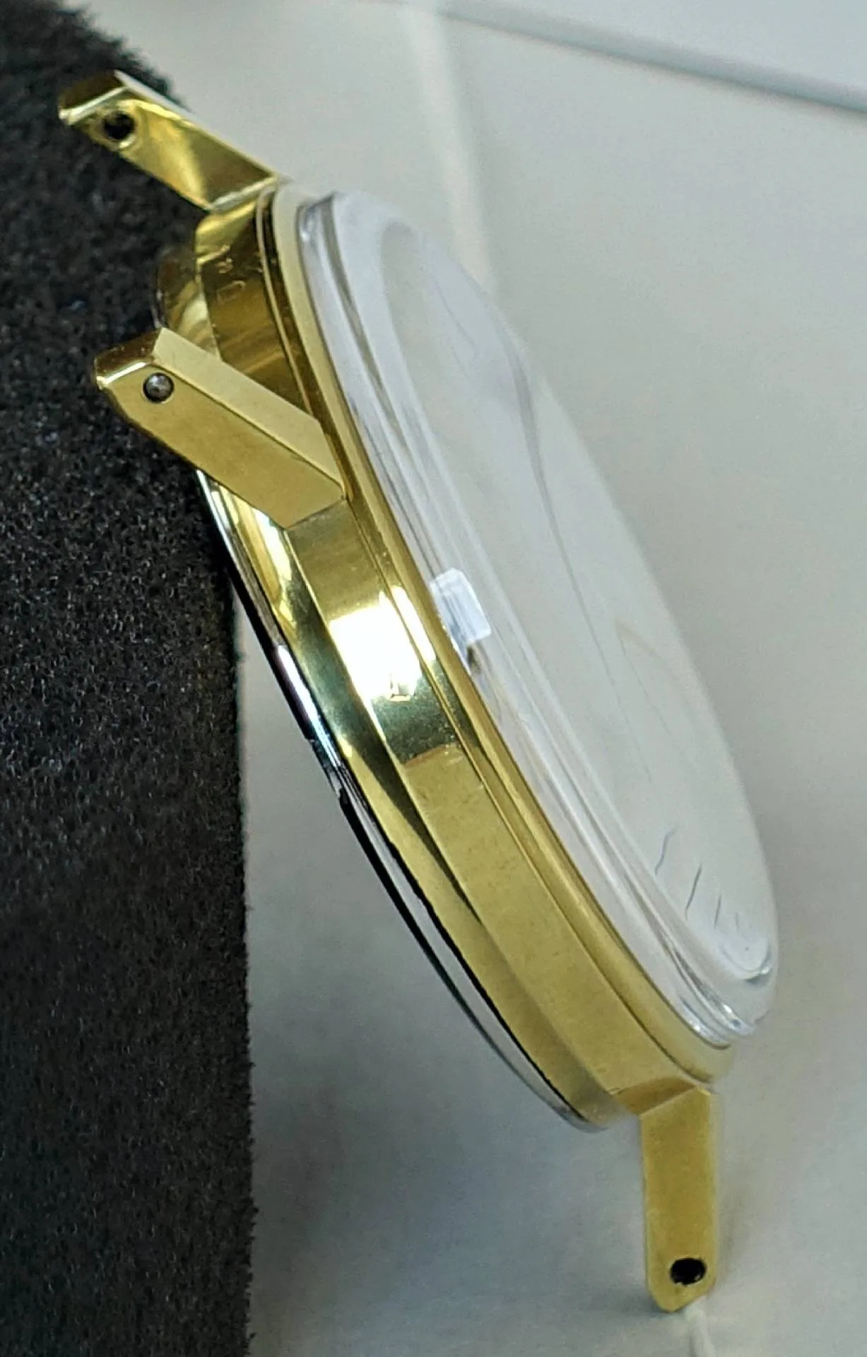 Rundes Uhrgehäuse in goldfarbener Optik mit angesetzten Bandanstößen und transparentem Uhrglas.