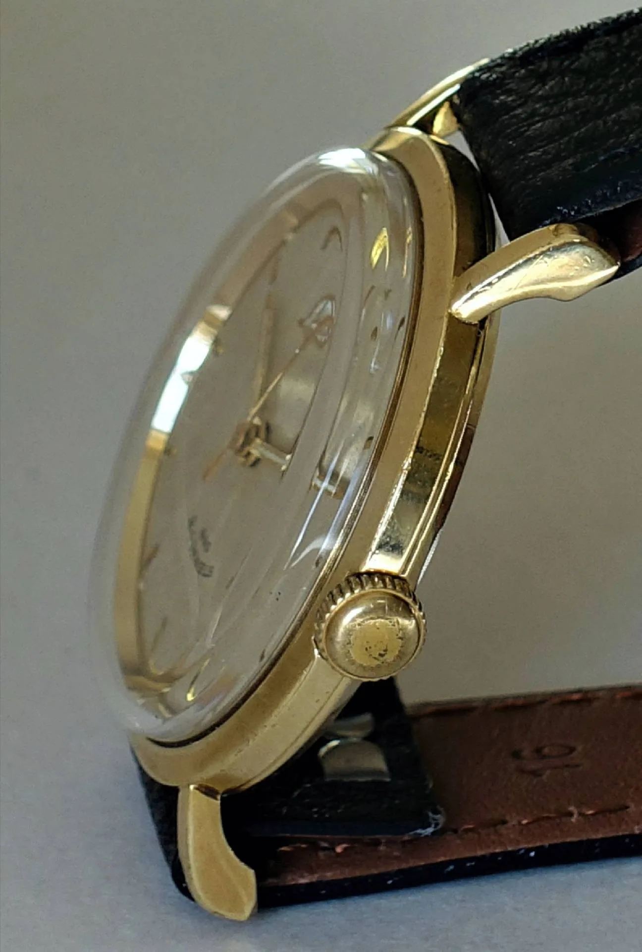 Analoge Armbanduhr mit goldfarbenem Gehäuse und schwarzem Lederarmband.