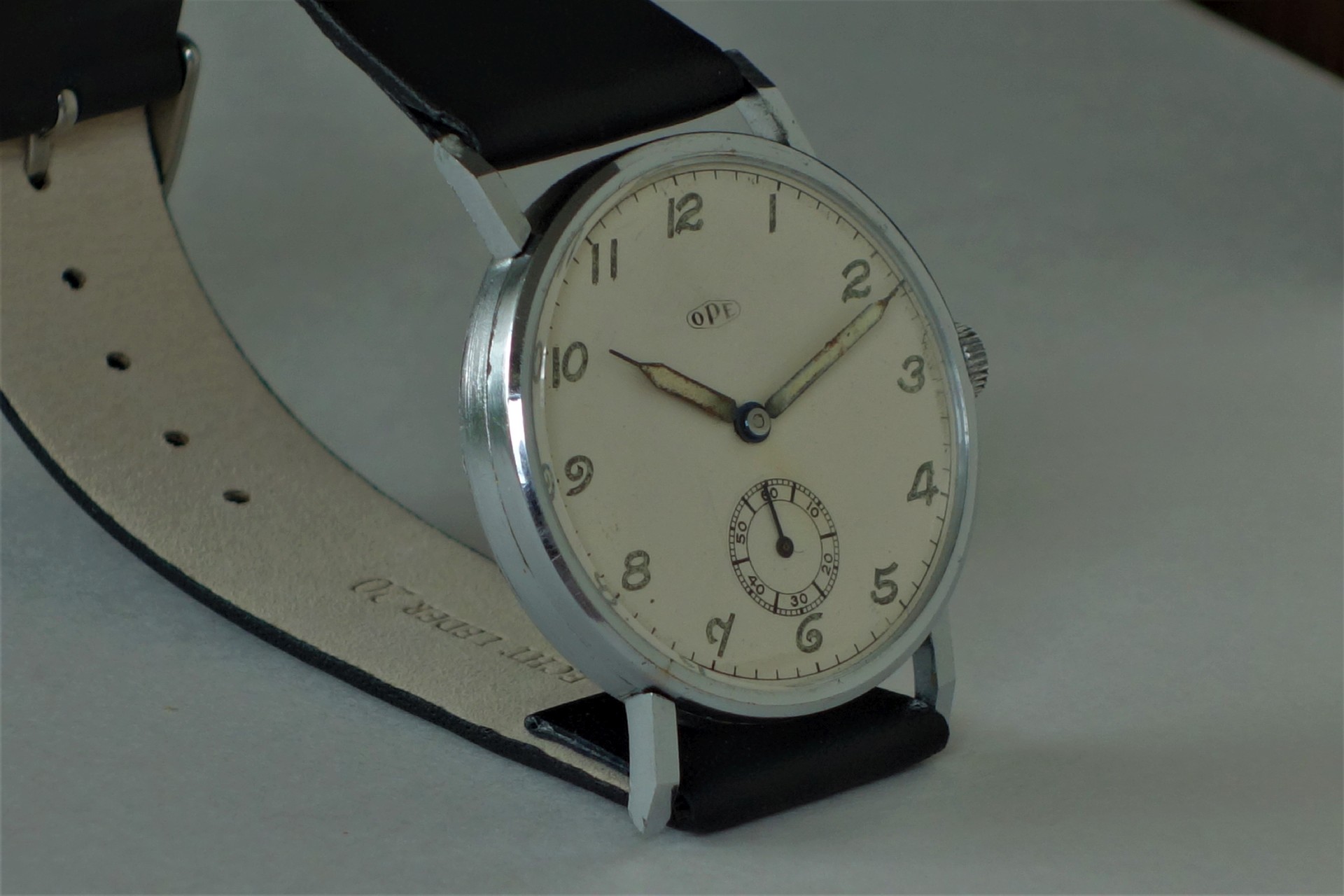 Analoge Armbanduhr mit hellem Zifferblatt und schwarzem Lederarmband.