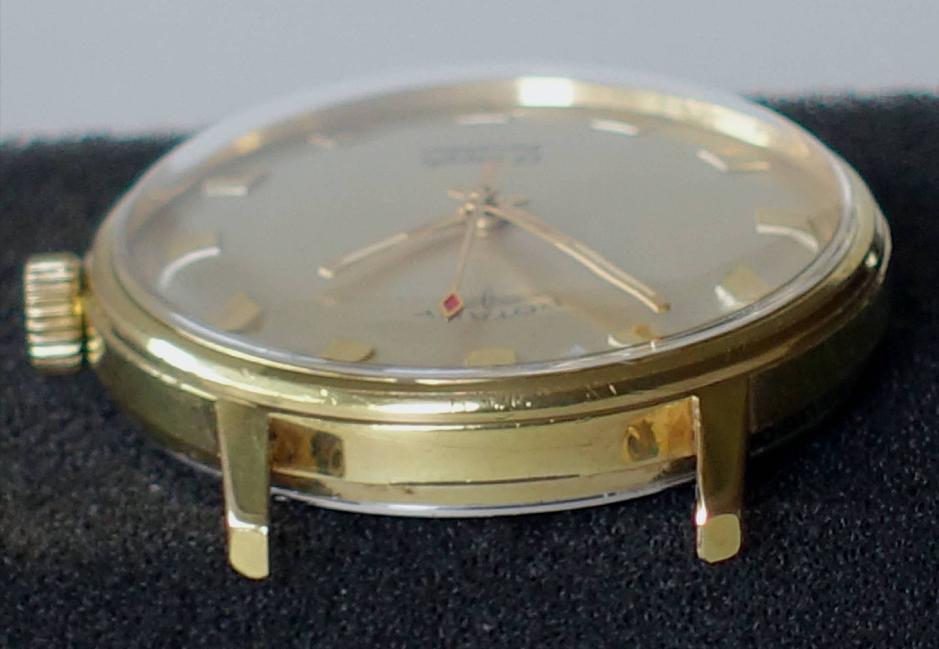 Flache Armbanduhr mit goldfarbenem Gehäuse und hellem Zifferblatt.
