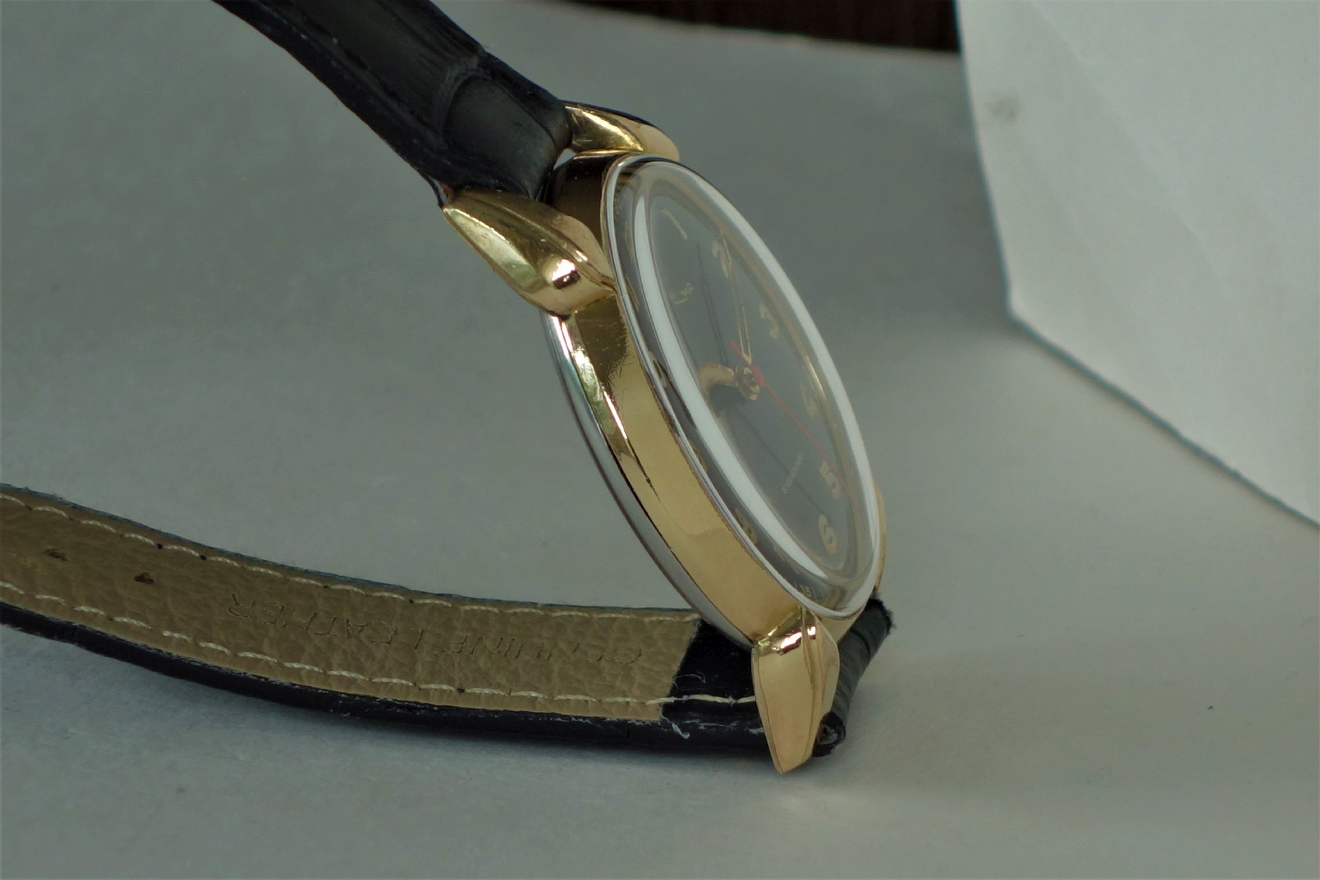 Armbanduhr mit goldfarbenem Gehäuse und schwarzem Lederarmband.