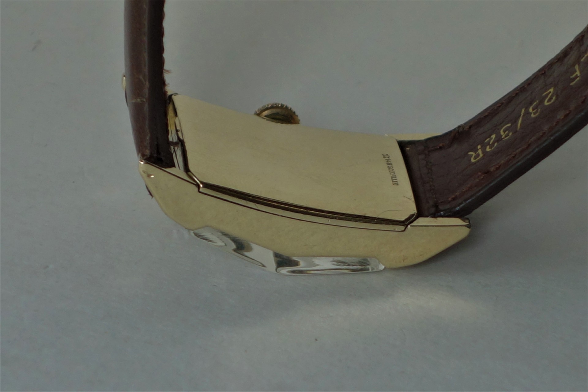 Rechteckiges Uhrgehäuse in goldfarbener Optik mit braunem Lederarmband.