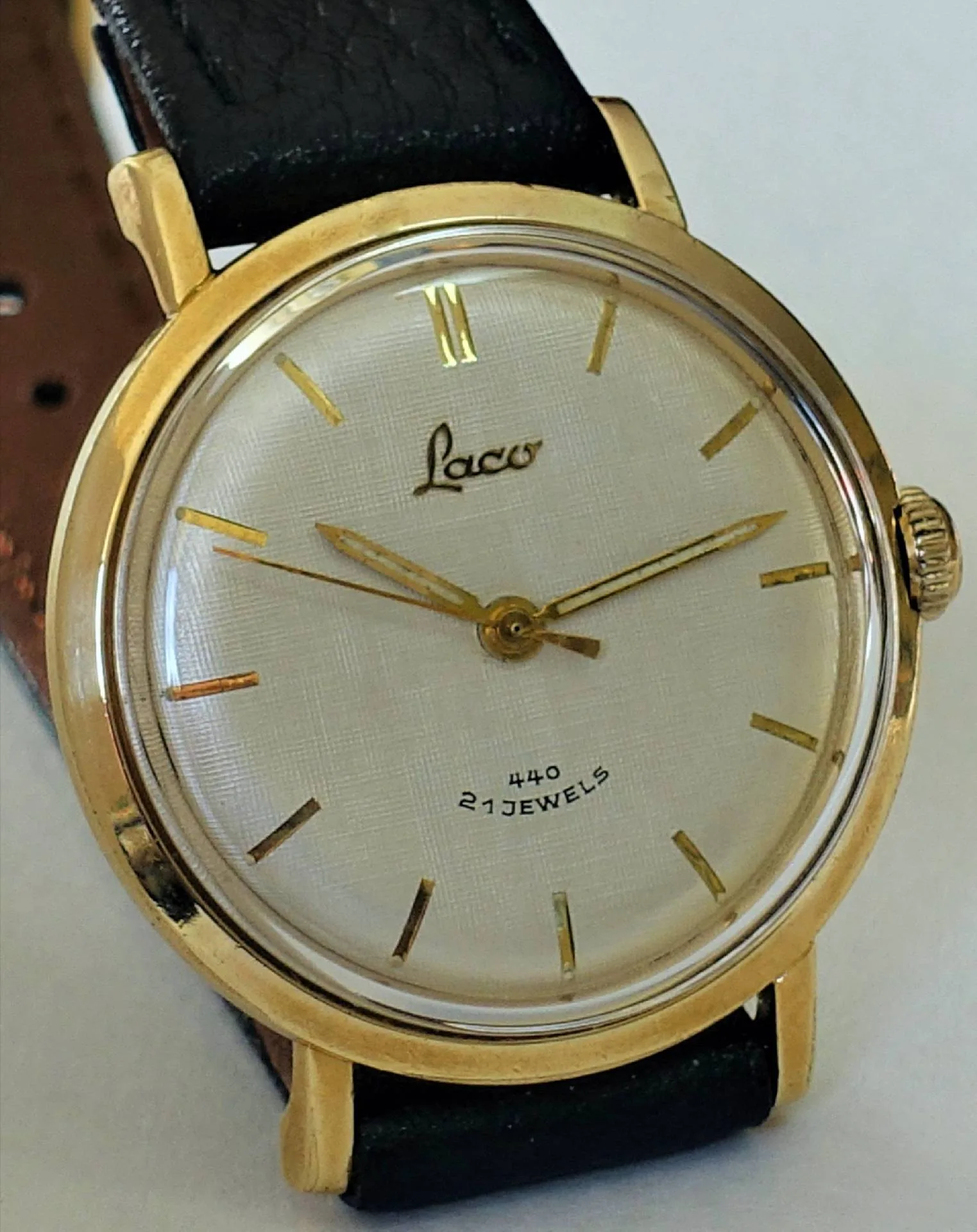 Goldfarbene Laco Armbanduhr mit hellem Zifferblatt und schwarzem Armband.
