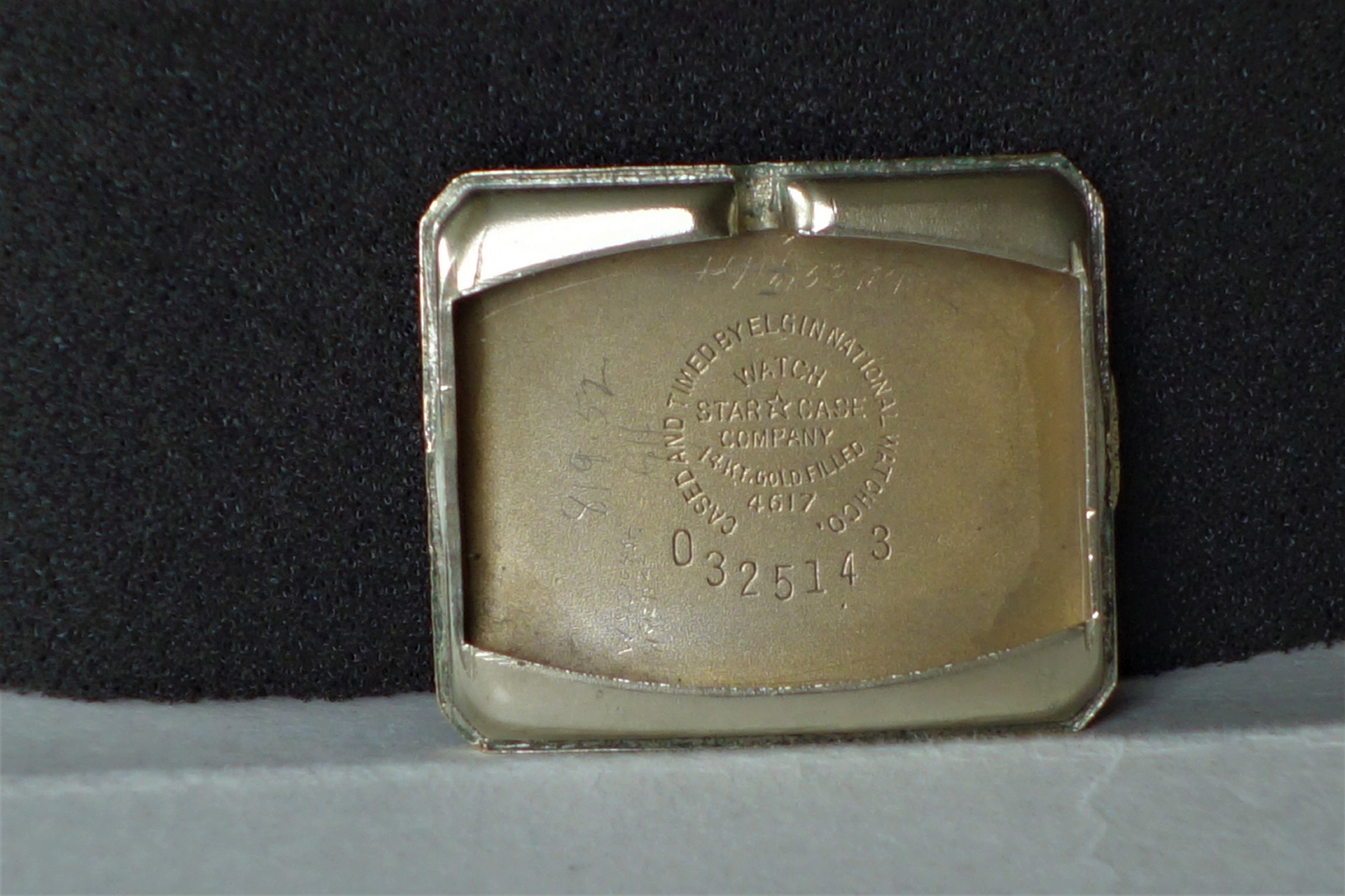 Rechteckiger goldfarbener Gehäuseboden für Armbanduhren mit Gravur und Seriennummer.
