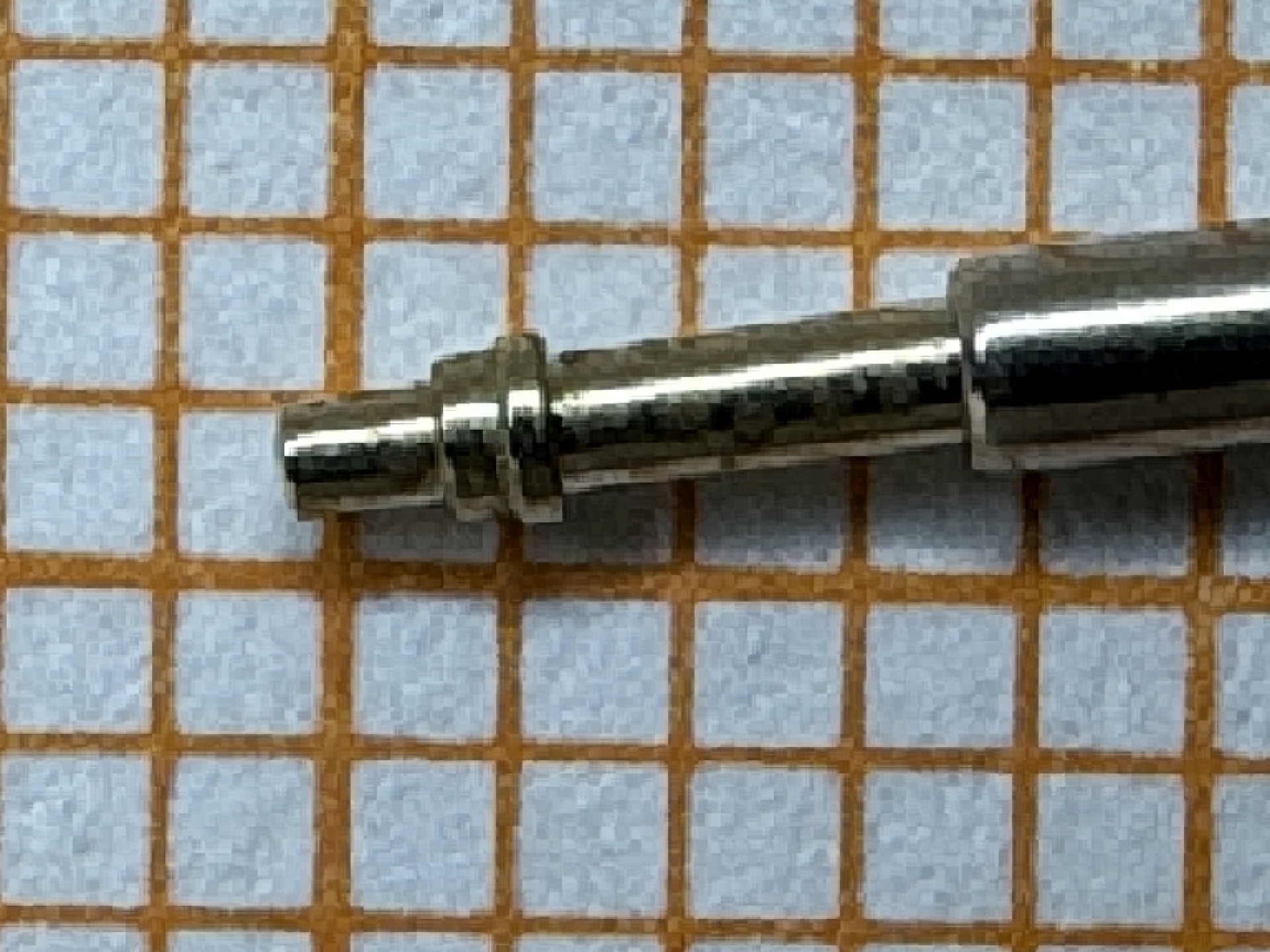 Metallische Aufzugswelle für Uhrwerke auf kariertem Papier.