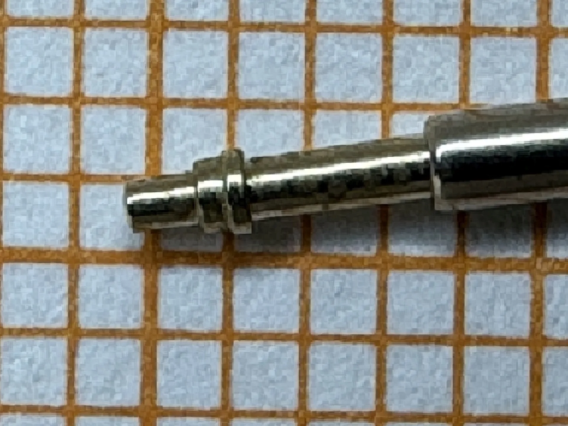 Metallische Aufzugswelle für Uhrwerke auf kariertem Papier.