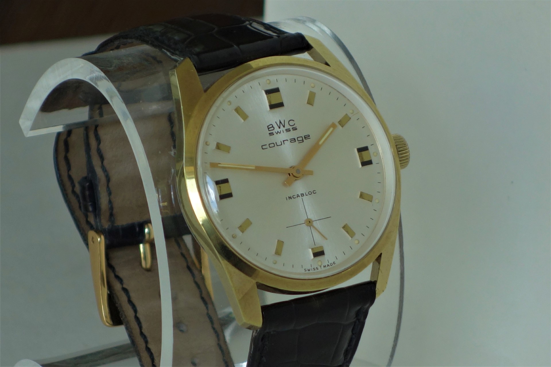 Klassische Armbanduhr mit goldfarbenem Gehäuse, hellem Zifferblatt und schwarzem Lederarmband.