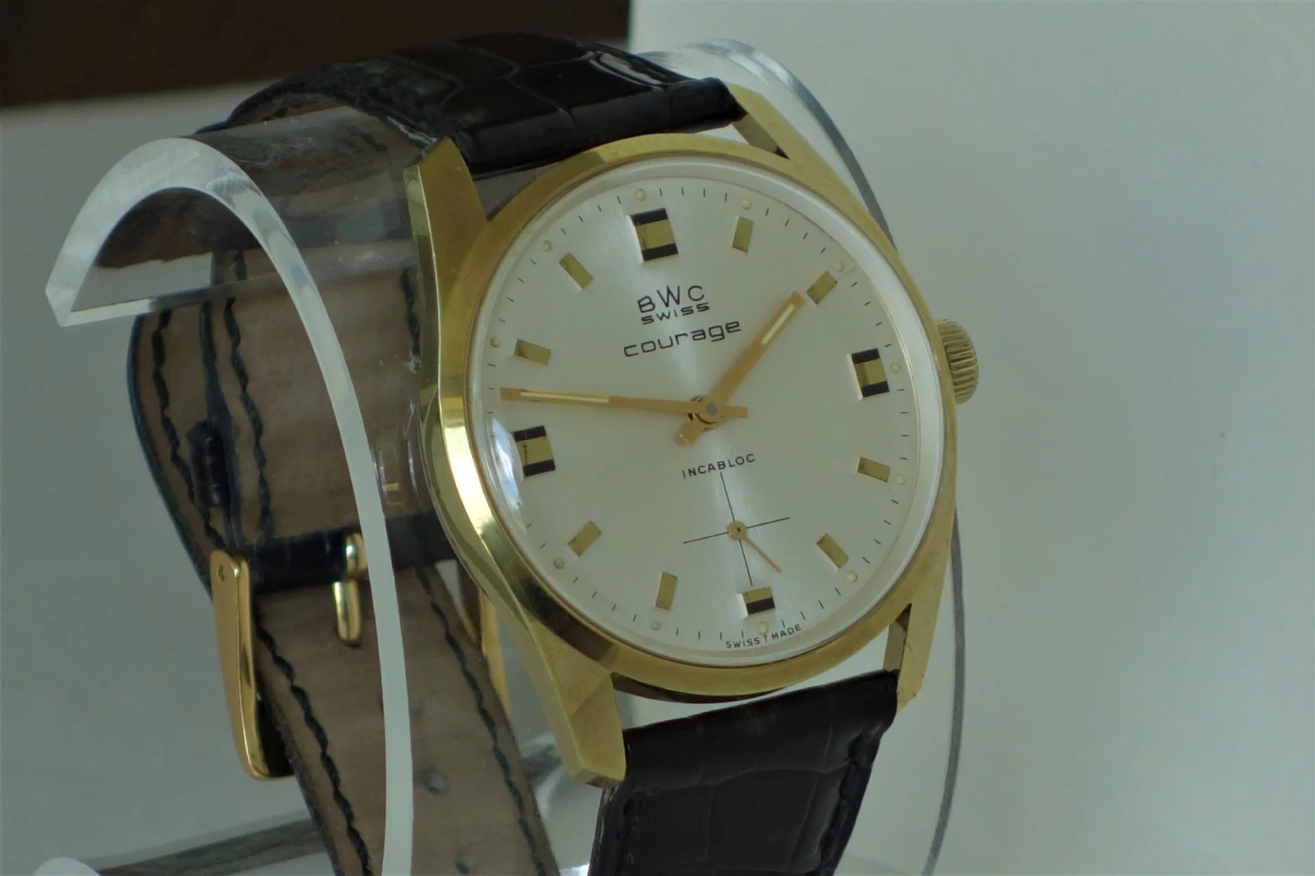 BWC Swiss Armbanduhr Klassische Armbanduhr mit goldfarbenem Gehäuse, hellem Zifferblatt und schwarzem Lederarmband.
