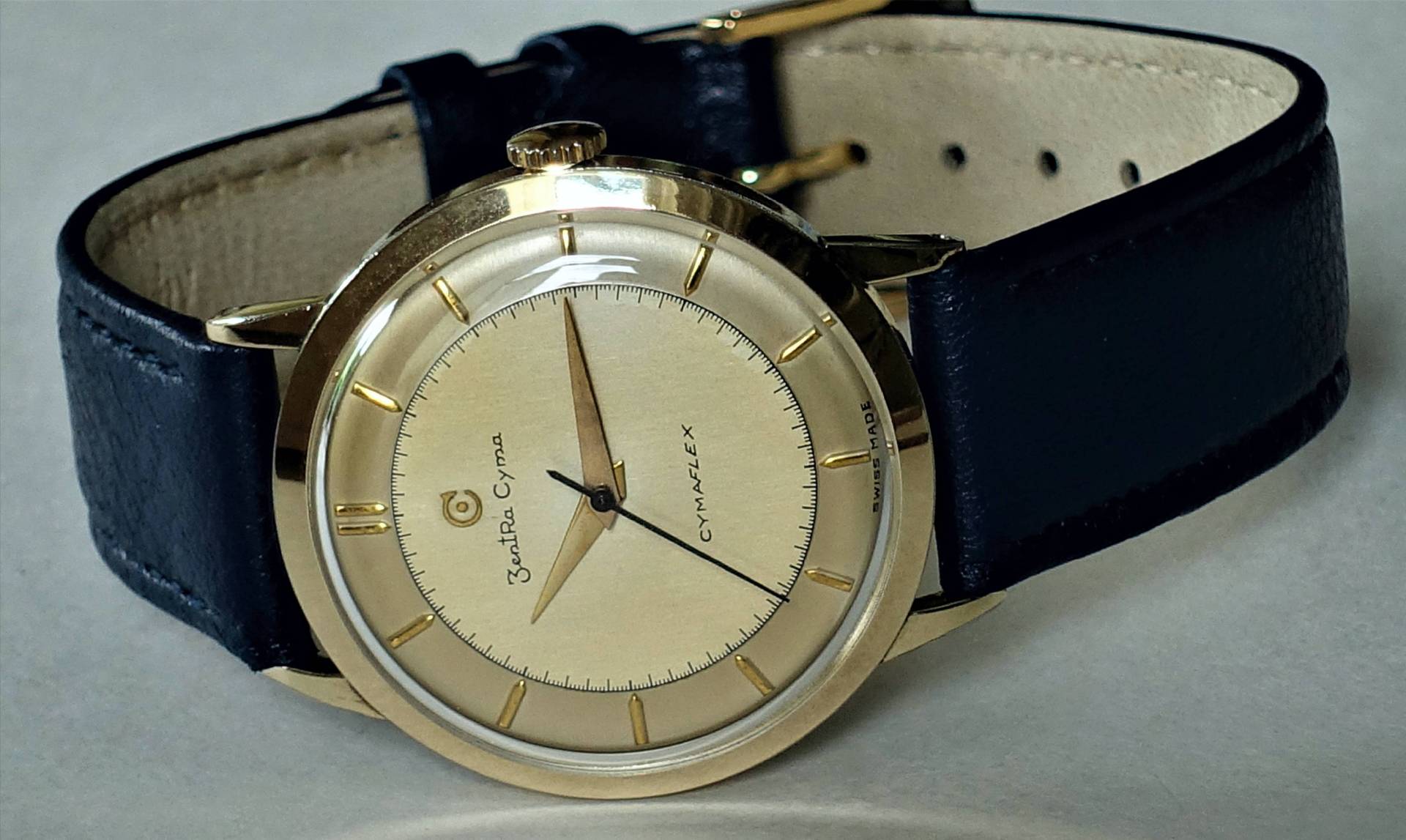 Goldfarbene Armbanduhr mit hellem Zifferblatt und schwarzem Lederarmband.