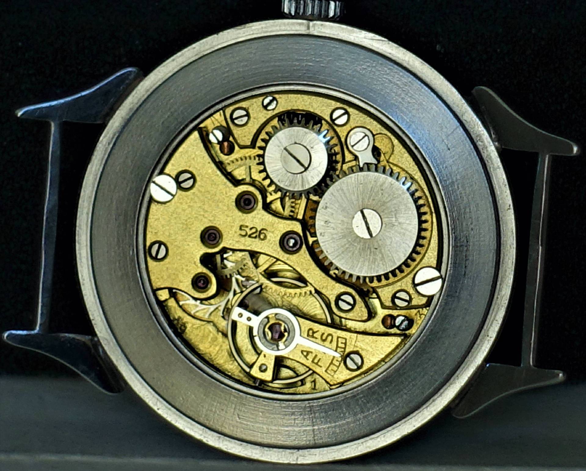 Mechanisches Uhrwerk in goldfarbener Ausführung mit sichtbaren Zahnrädern und Schrauben in einem silberfarbenen Gehäuse.