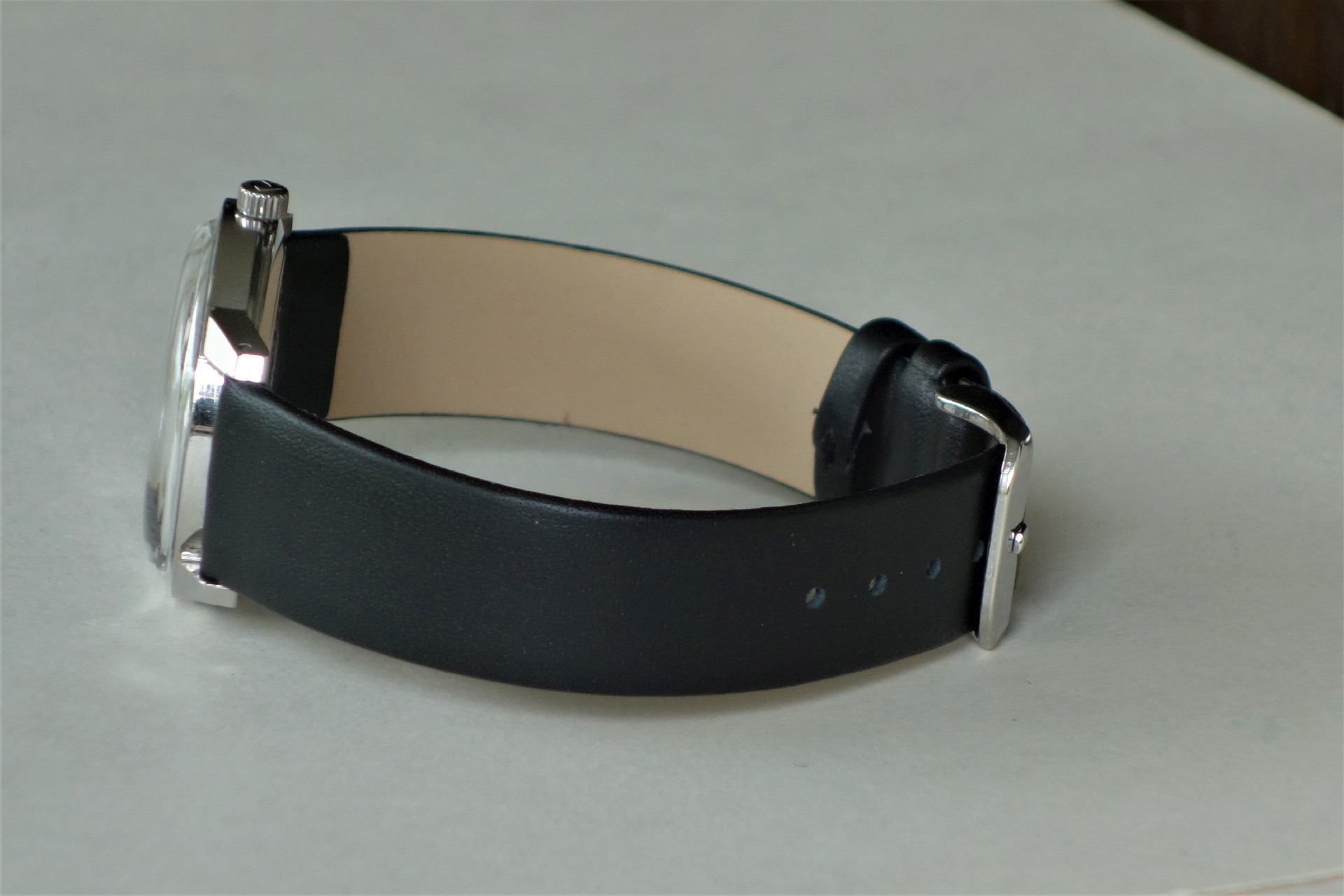 Schwarzes Lederarmband mit silberfarbener Schließe an einer Armbanduhr.