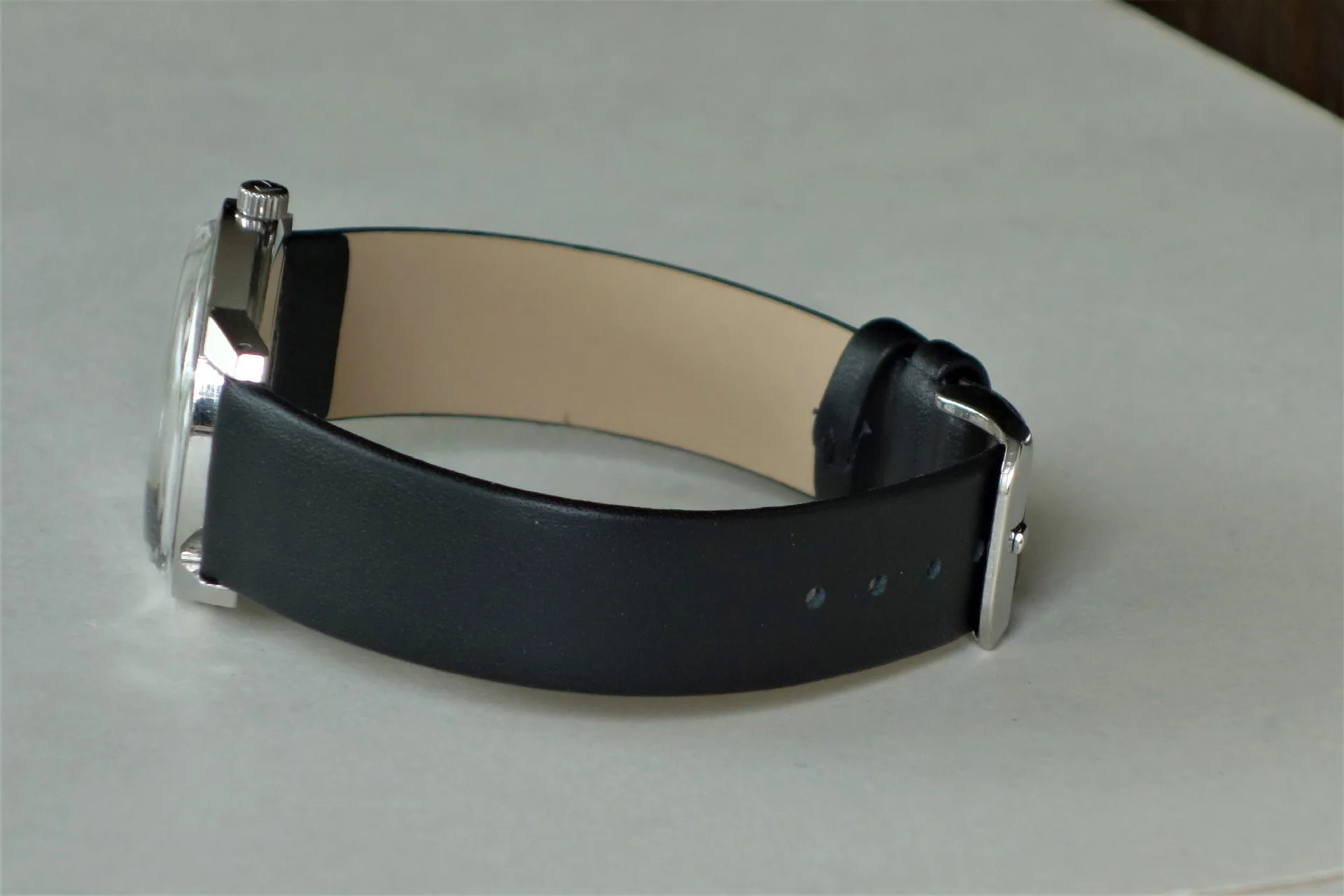 Schwarzes Lederarmband mit silberfarbener Schließe an einer Armbanduhr.