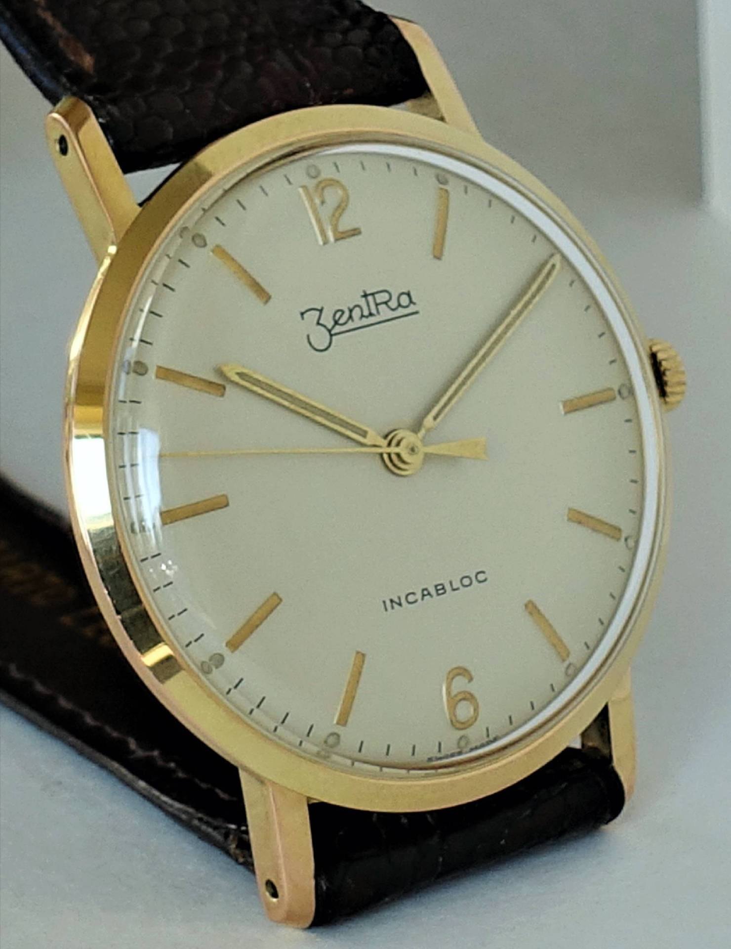 Klassische Armbanduhr mit goldfarbenem Gehäuse, hellem Zifferblatt und schwarzem Armband.