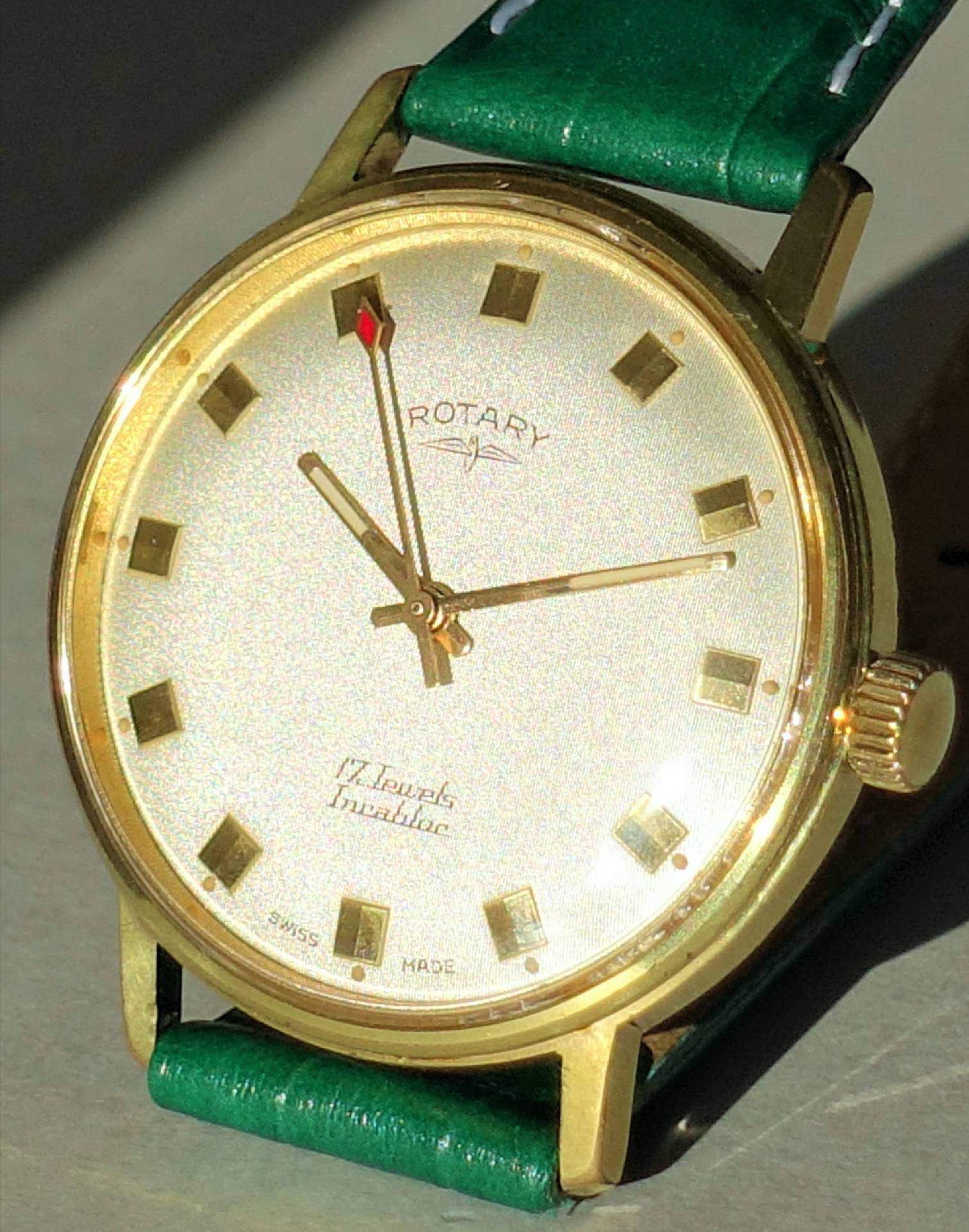 Goldfarbene Armbanduhr mit weißem Zifferblatt und grünem Armband.